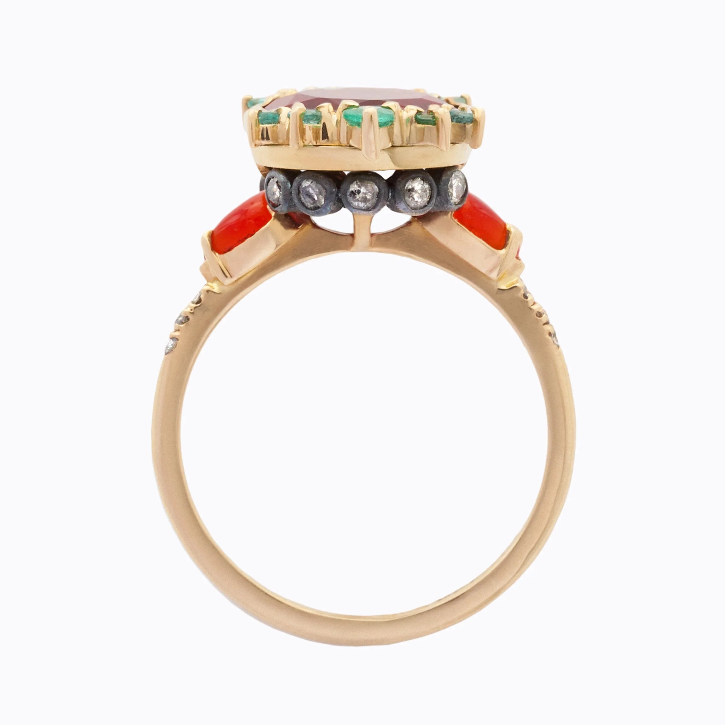 A vintage-style yellow gold ring featuring a large oval red center stone, accented with green and diamond stones, orange pear side stones, and a smooth gold band on a light gray background.