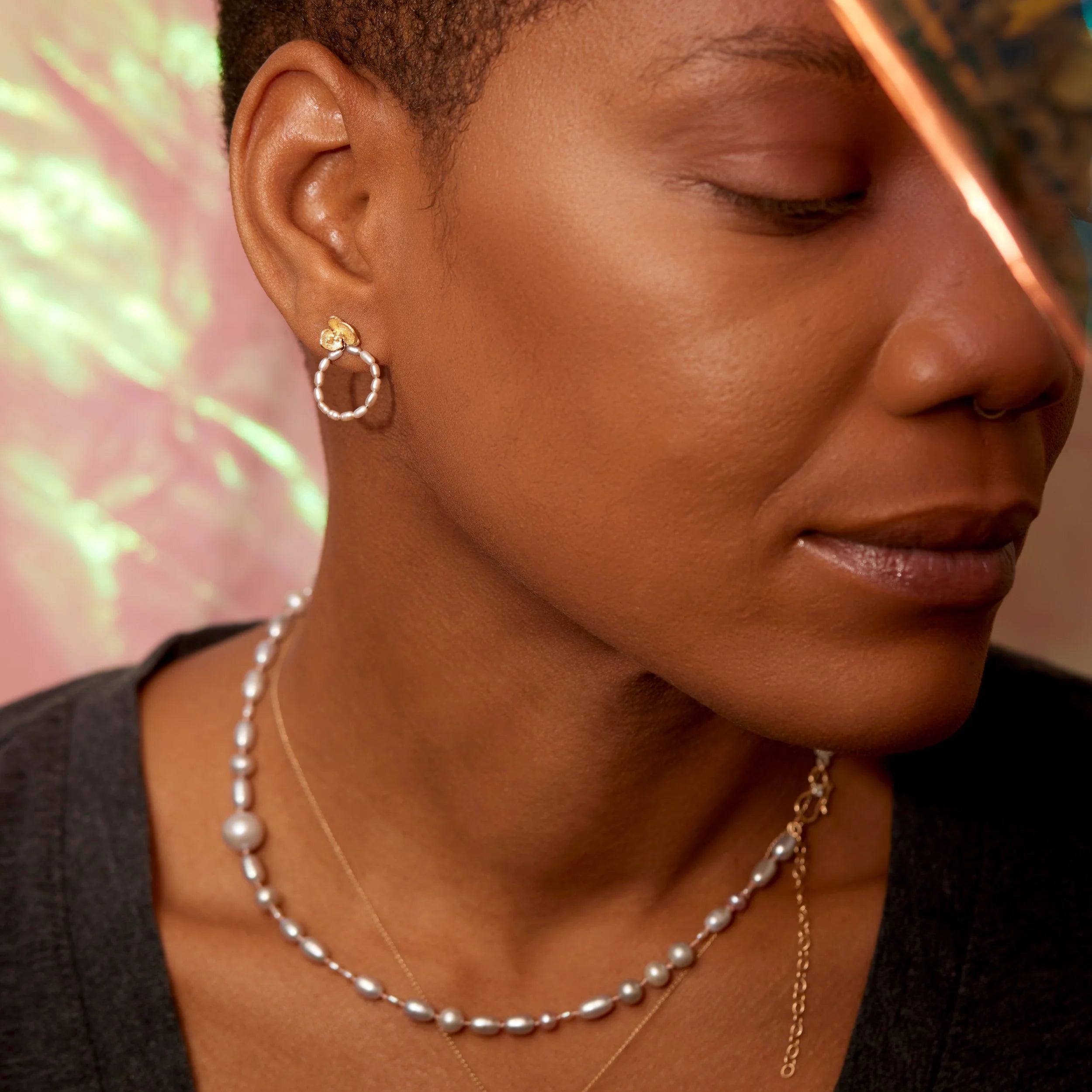 Close-up of a woman wearing gold hoop earrings and a pearl necklace with a blurred background