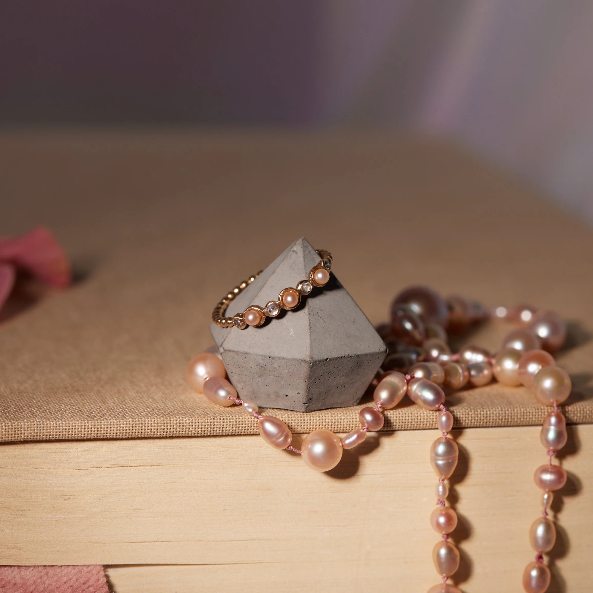 Pearl necklace and ring with a geometric concrete holder on a textured surface