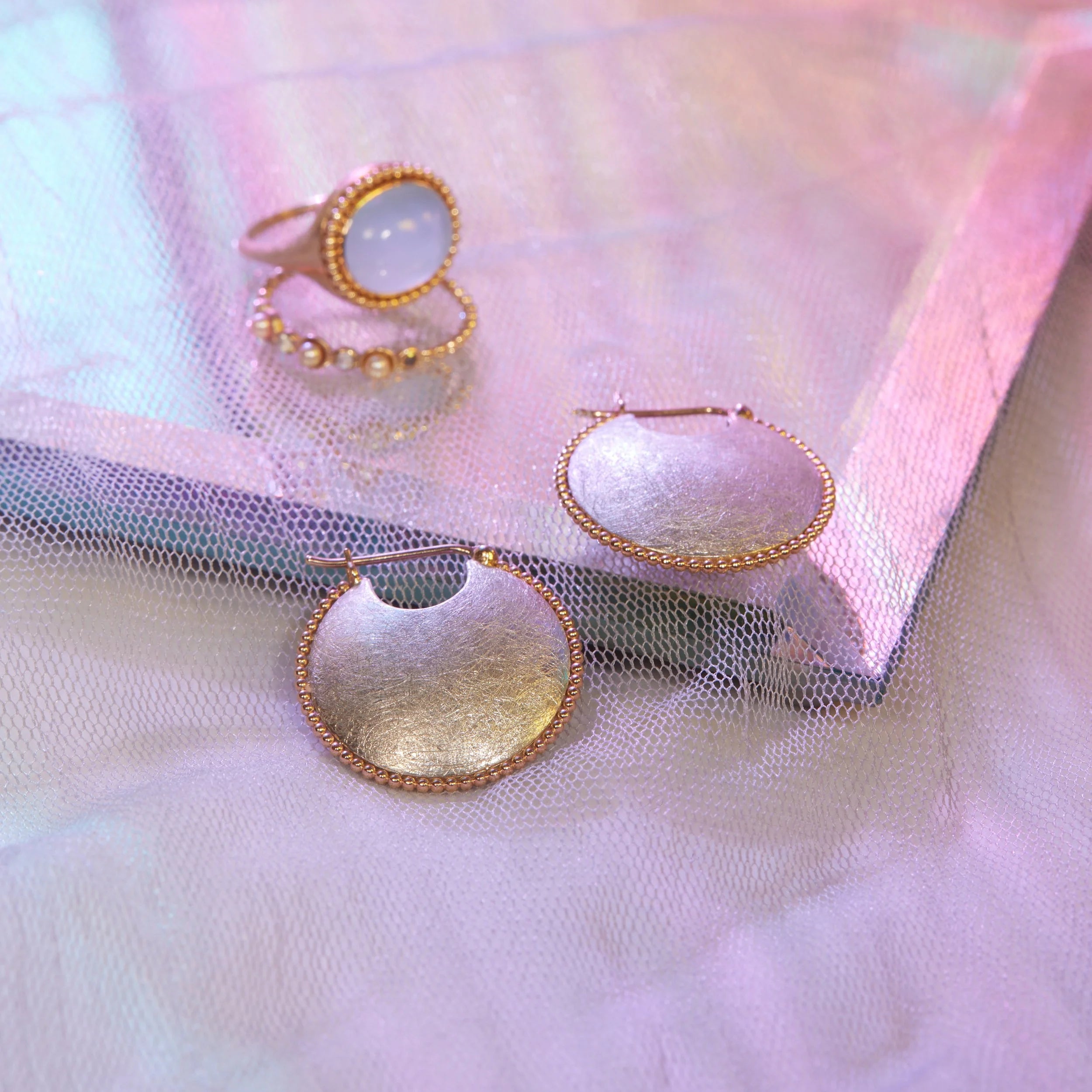 Gold and silver hoop earrings and ring on a soft fabric background