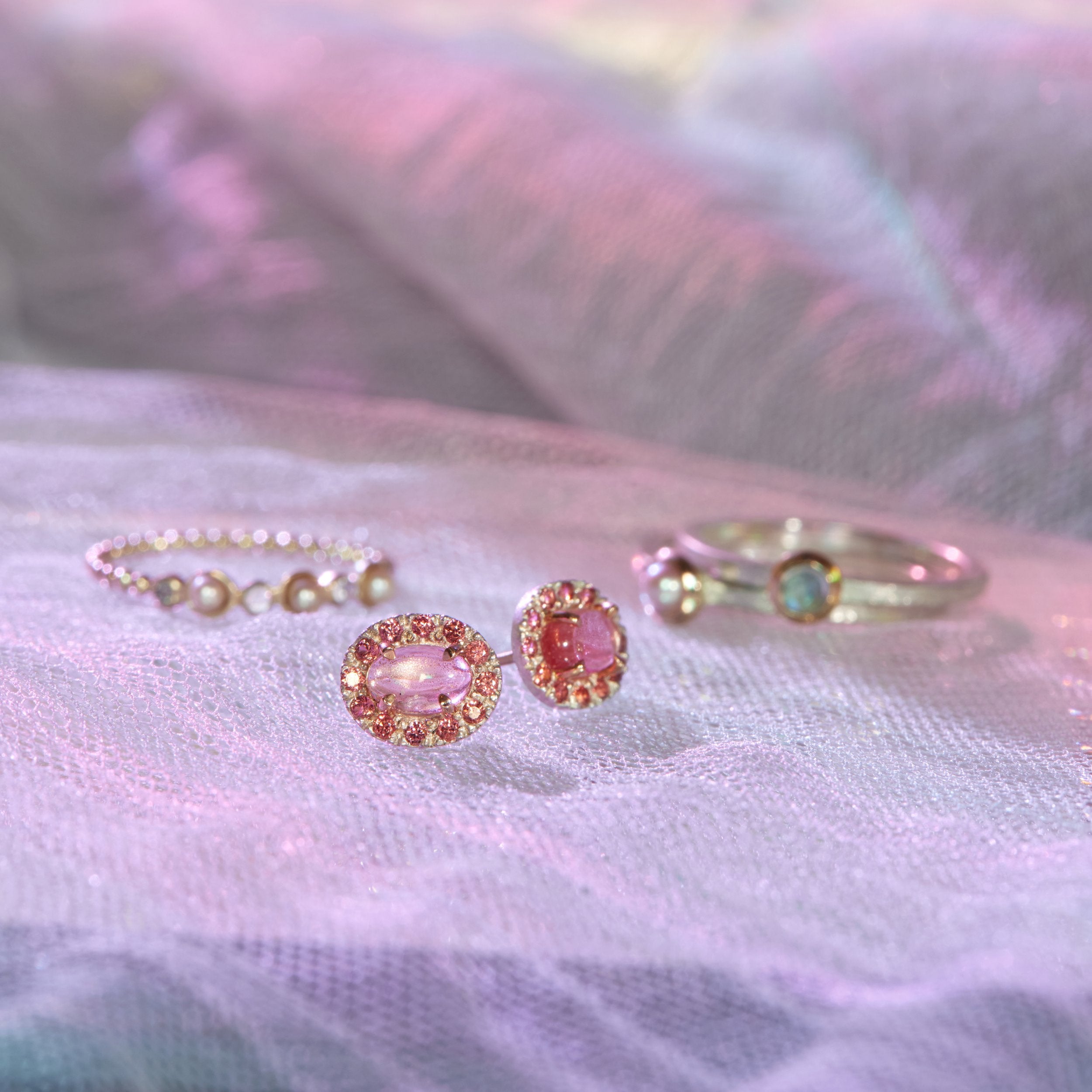 Pair of pink gemstone earrings with gold accents on a textured fabric background