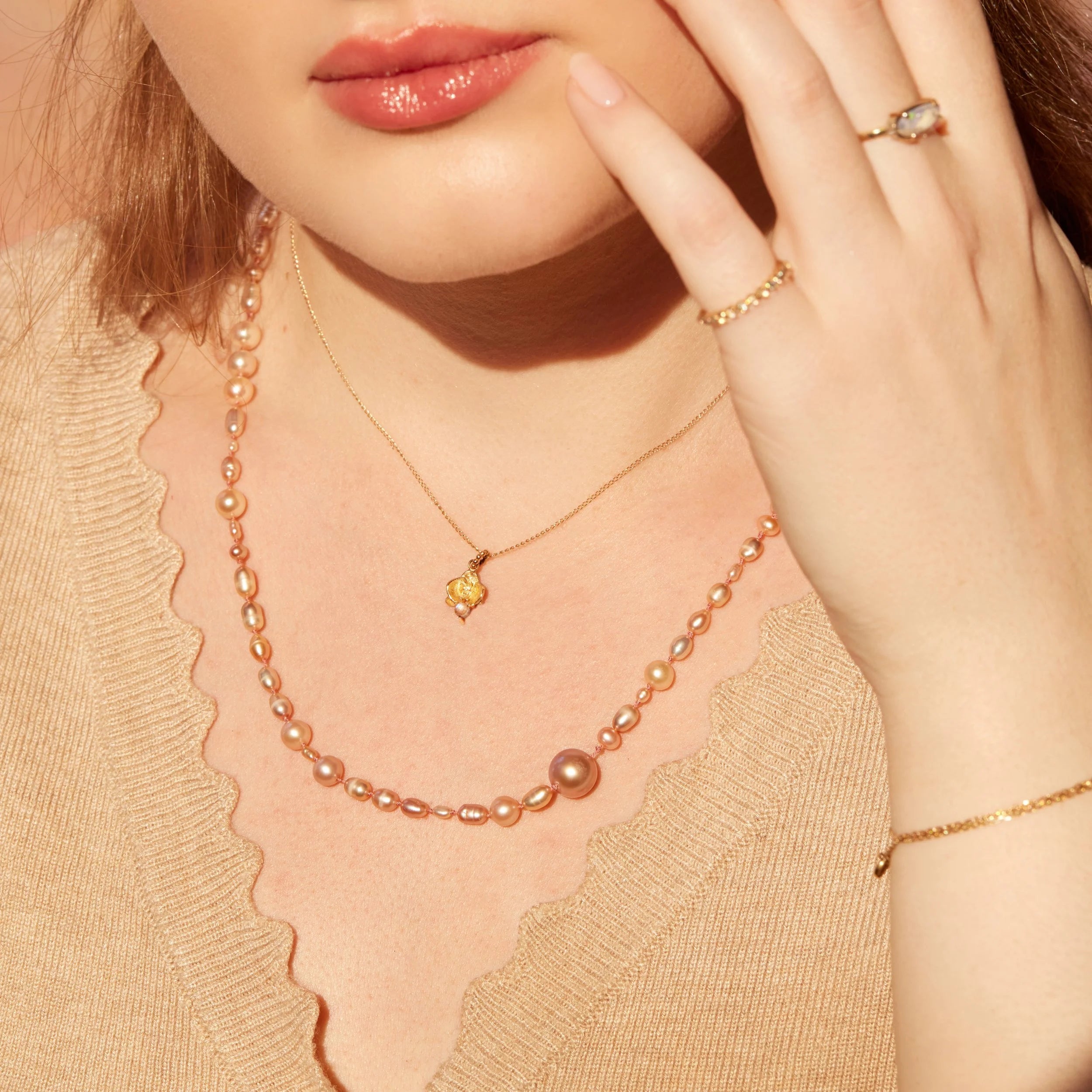 Close-up of a woman wearing a gold necklace with a floral pendant and pearl strands.