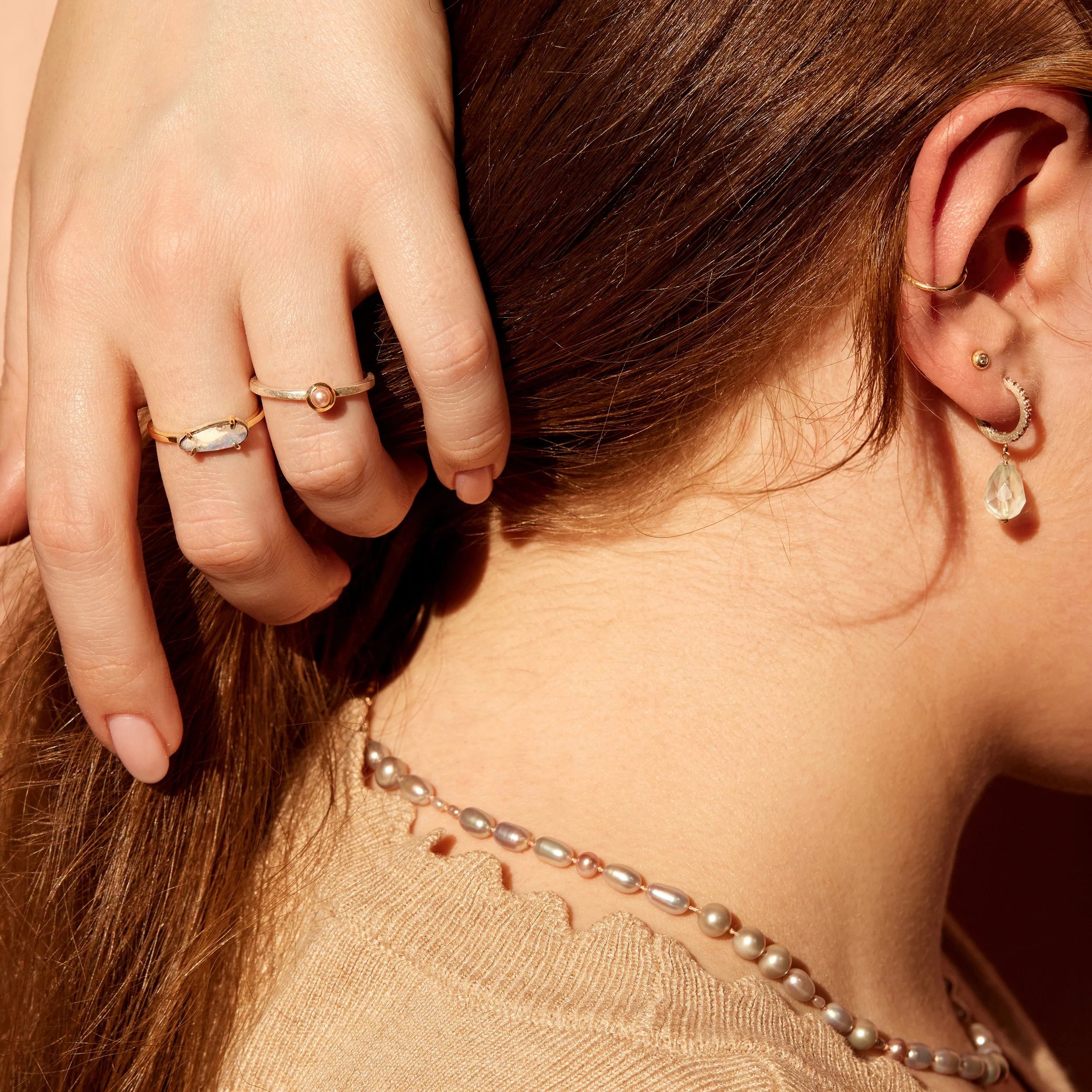 Close-up of a person wearing gold rings and earrings with a pearl necklace.