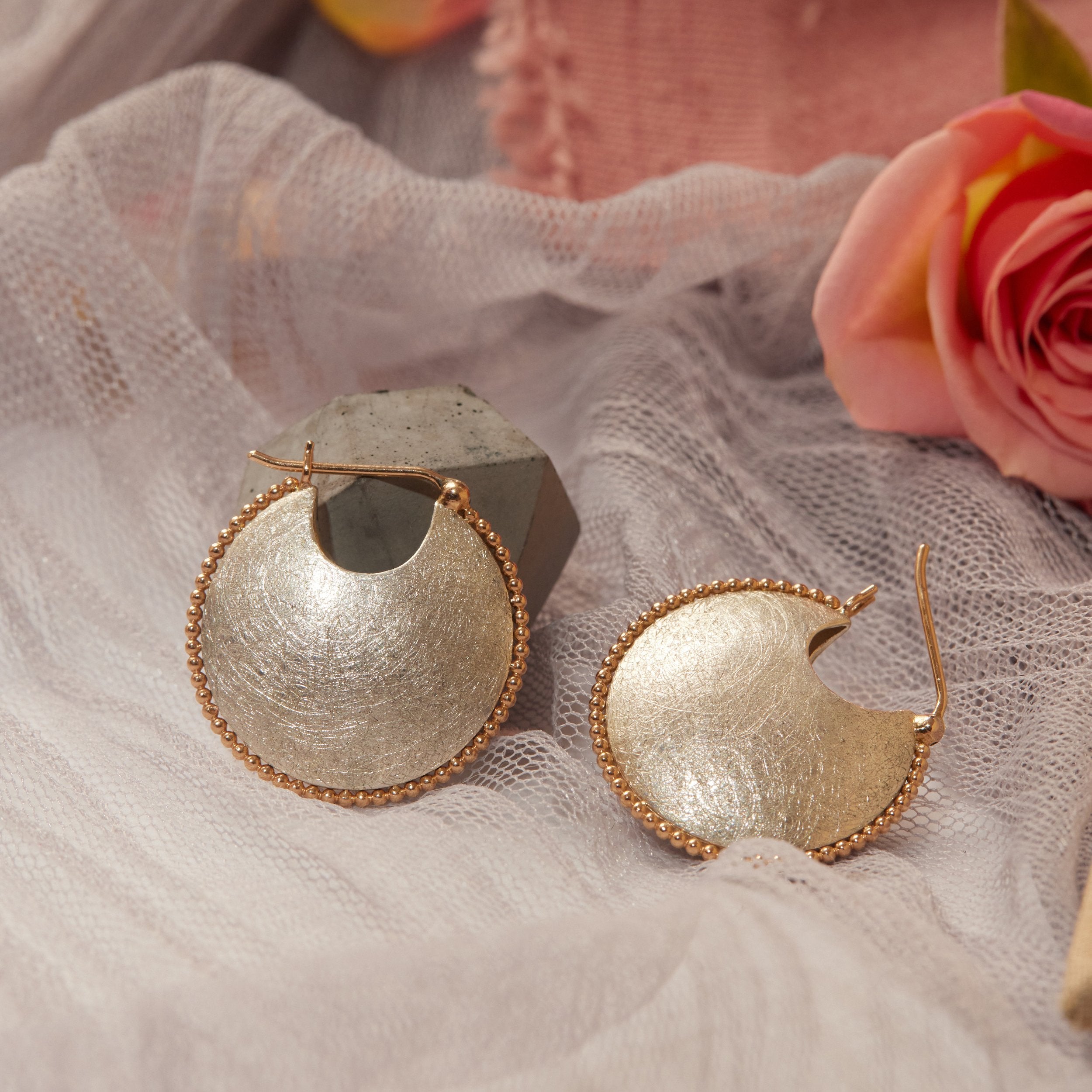 Gold and silver earrings on a soft fabric background with a pink flower.