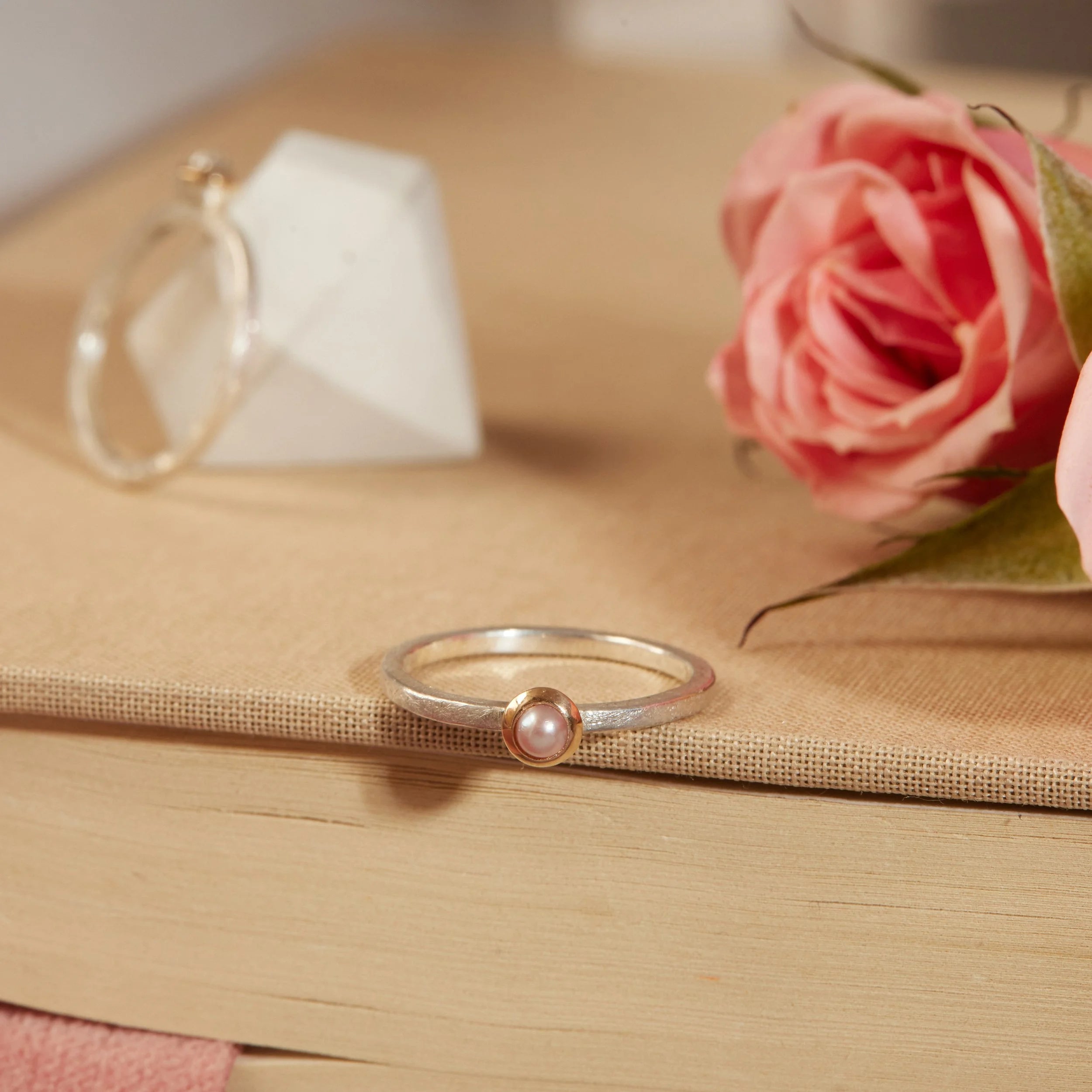 Silver ring with a pink gemstone on a book with a pink rose and tea cup in the background
