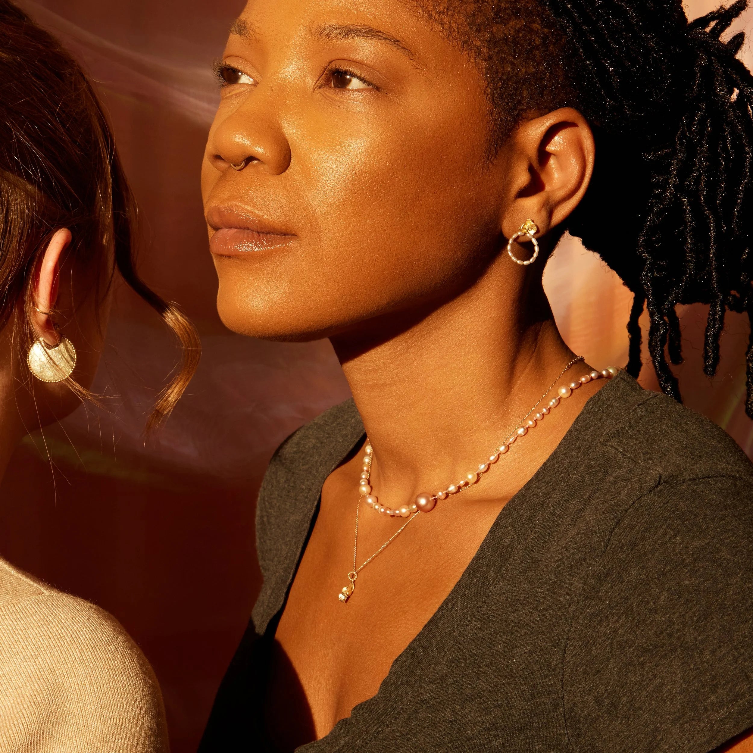 Close-up of a woman wearing earrings and a necklace with a warm, soft light background.