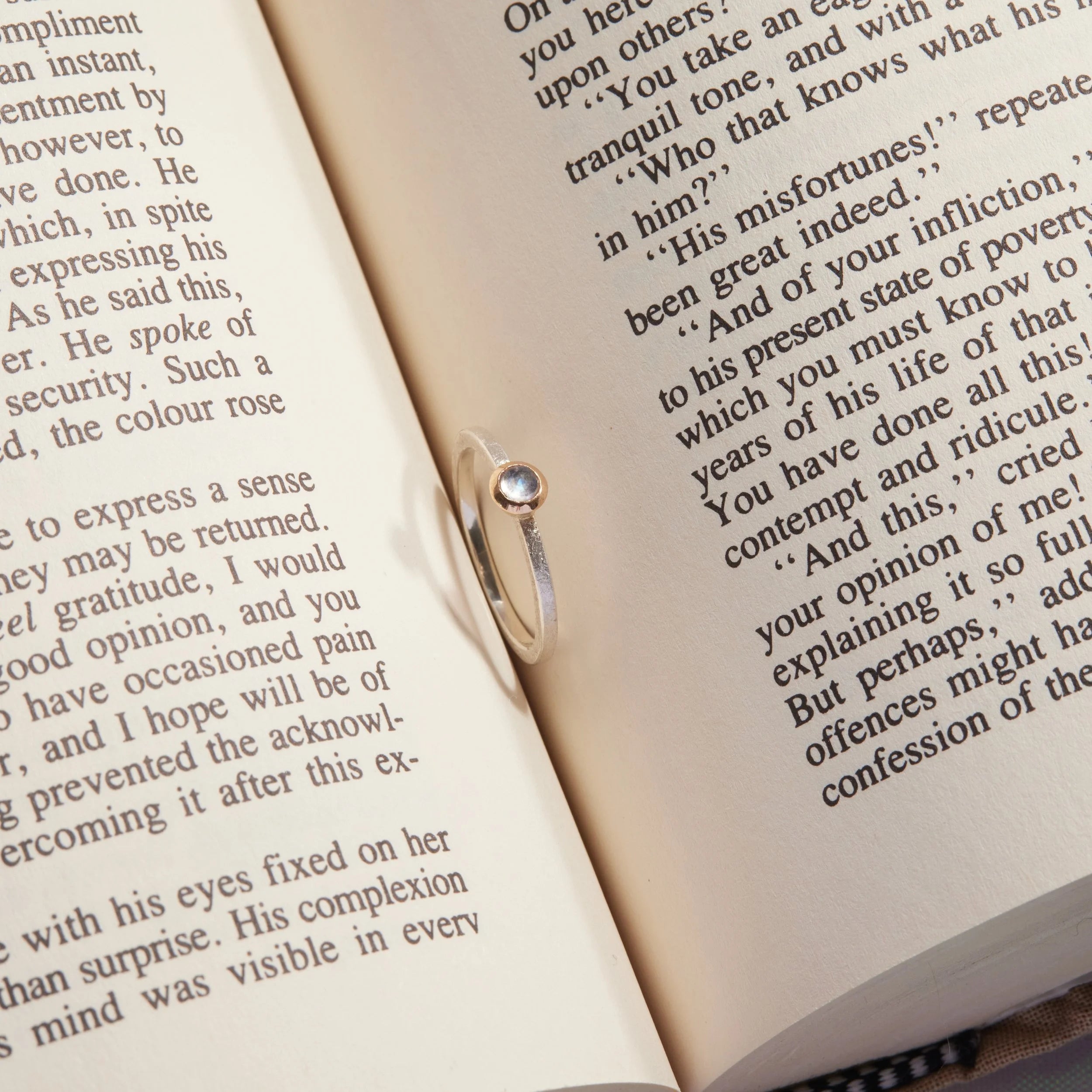 Open book with text, focus on a silver and gold moonstone ring