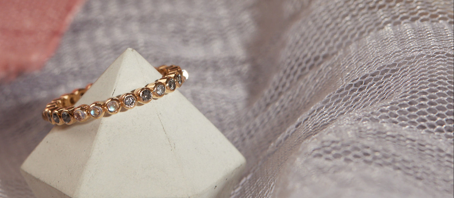 Gold ring with small stones on a white pyramid block against a textured fabric background