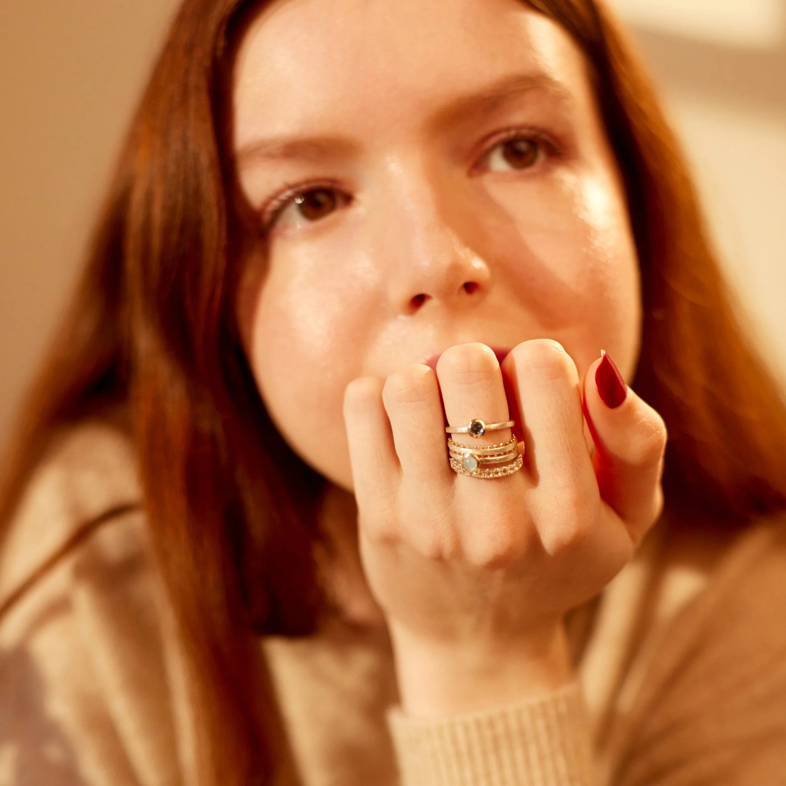Woman with rings on her fingers holding her hand near her mouth against a warm-toned background
