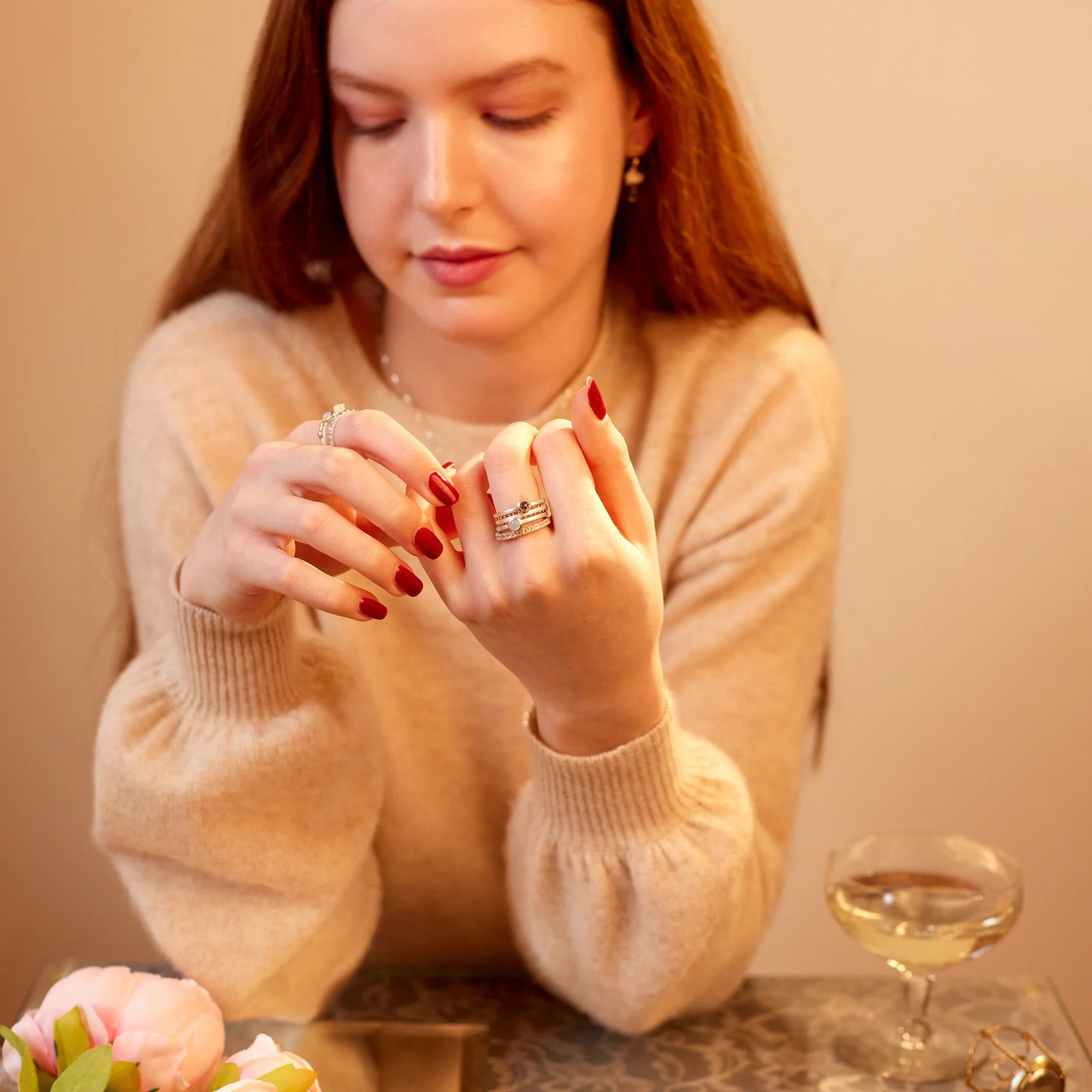 Woman examining jewelry with a glass of wine and flowers in the background