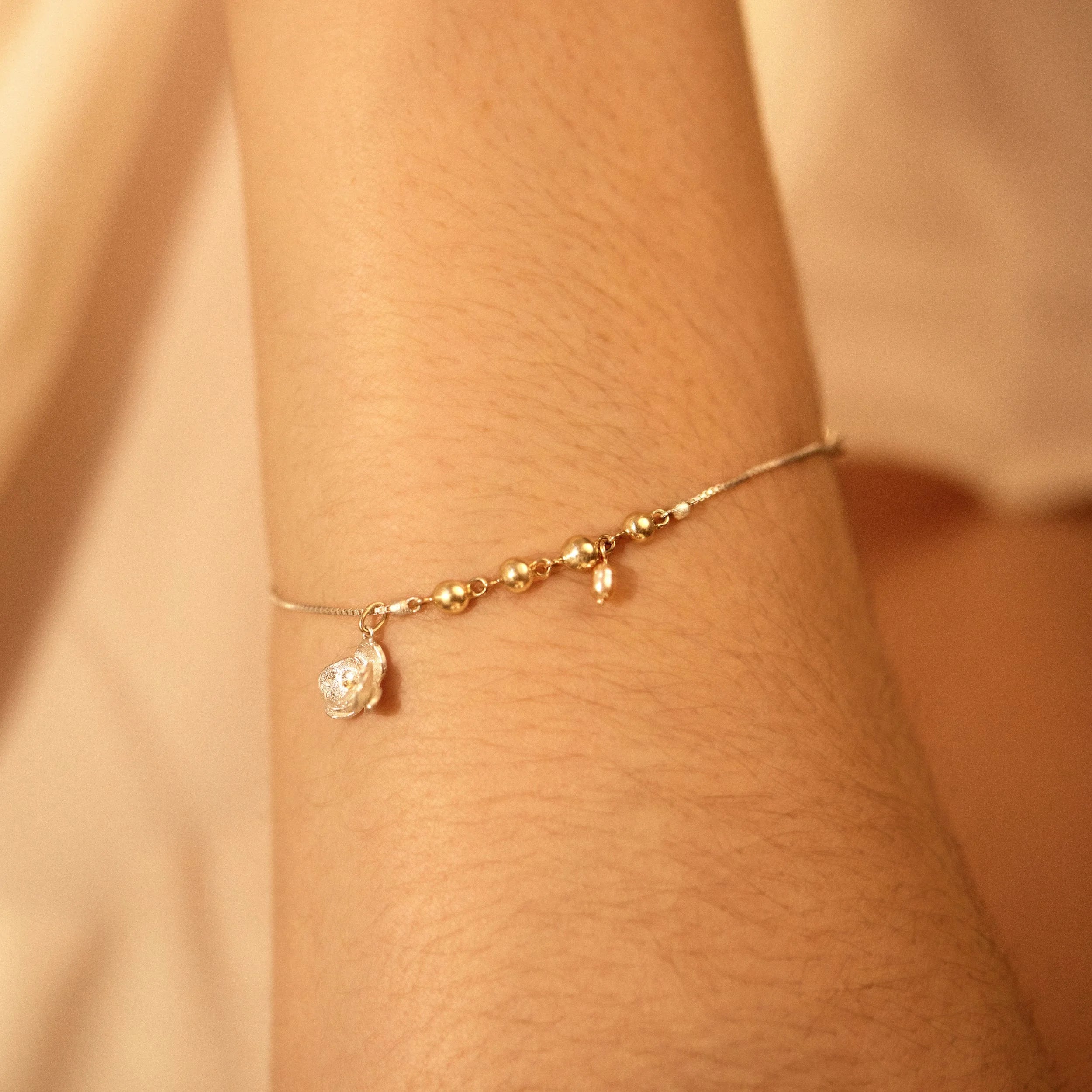 Gold and silver chain bracelet with a small charm on a person's wrist against a beige background