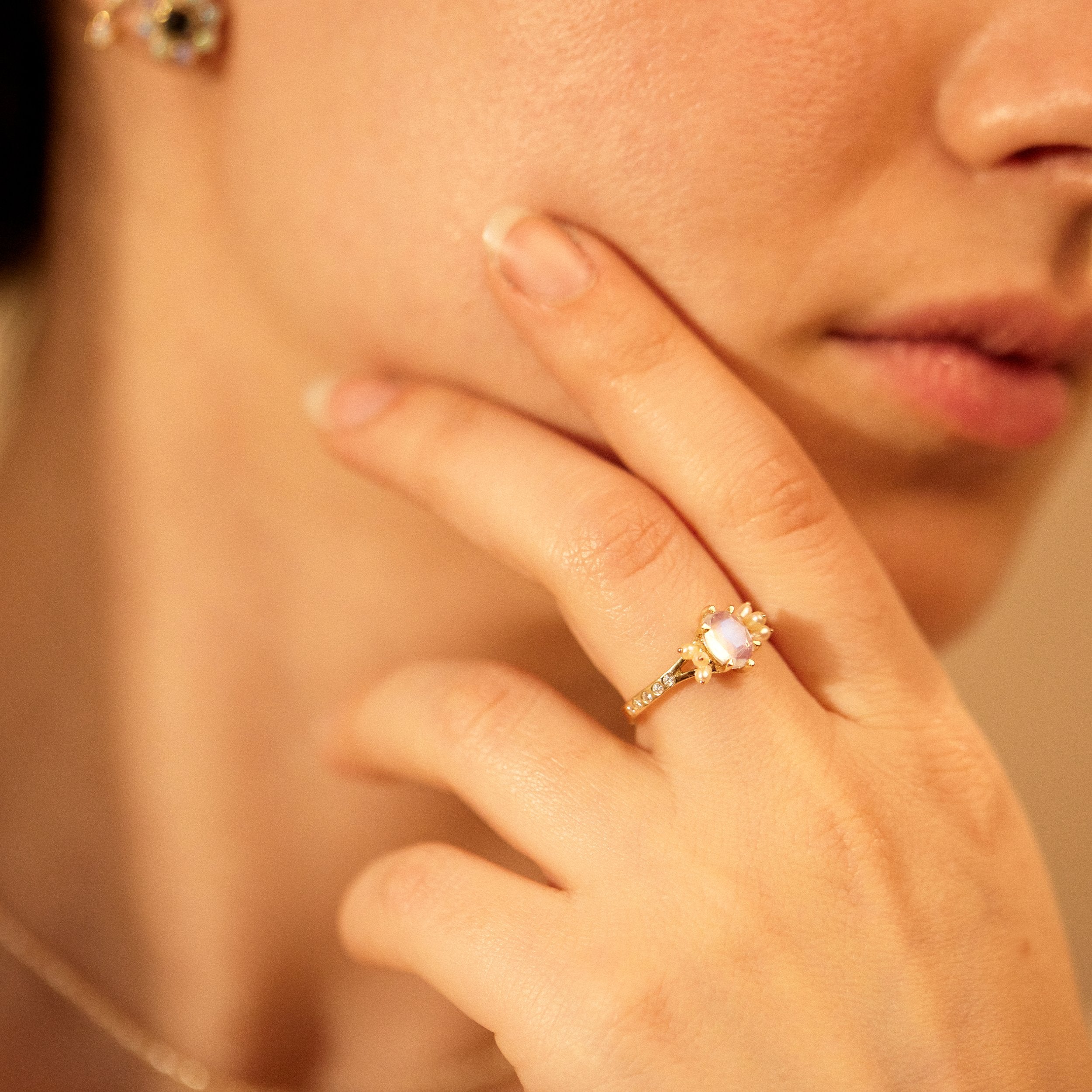 Close-up of a hand wearing a gold ring with a pink gemstone, touching the face.