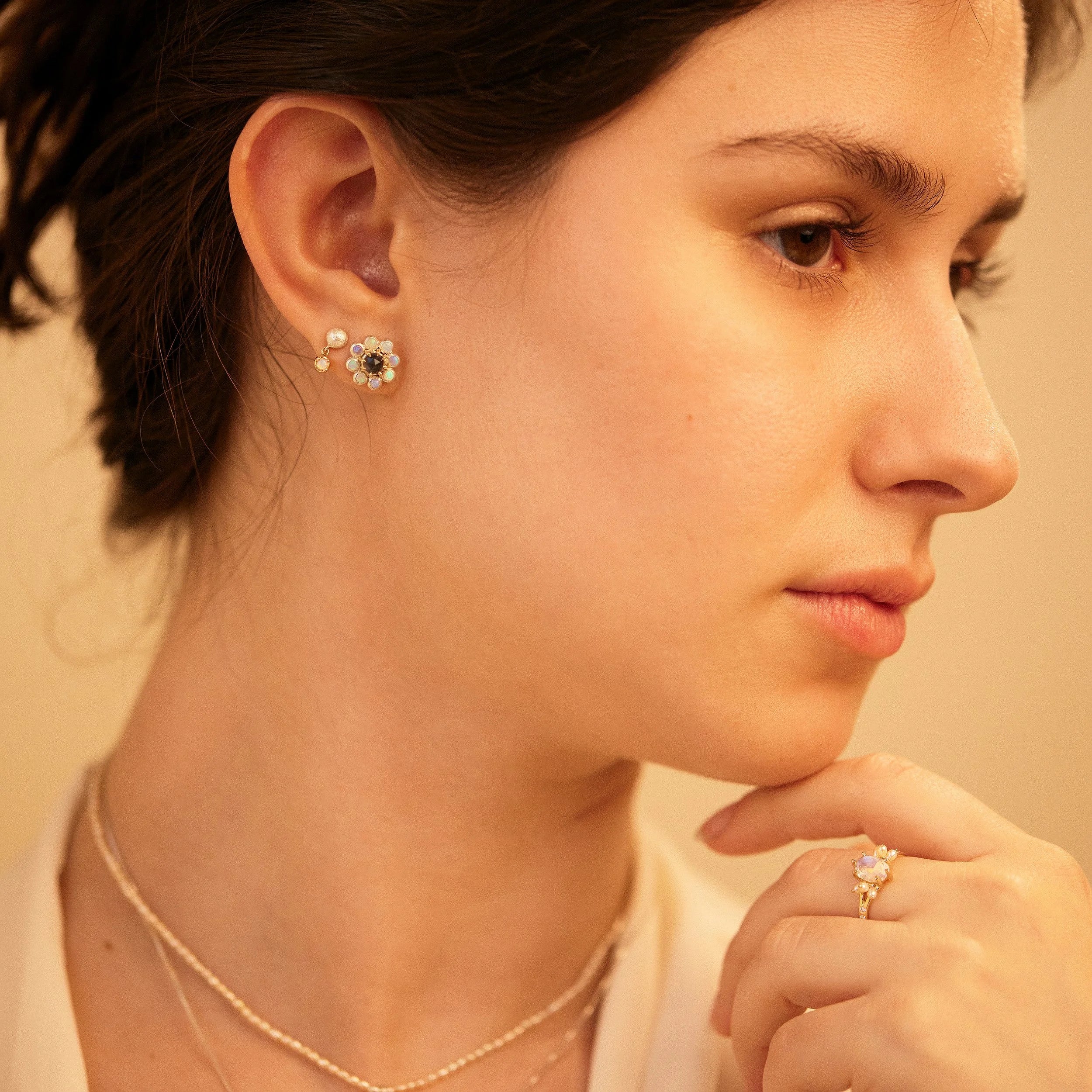 Close-up of a woman wearing earrings and a ring with a warm, soft focus background.