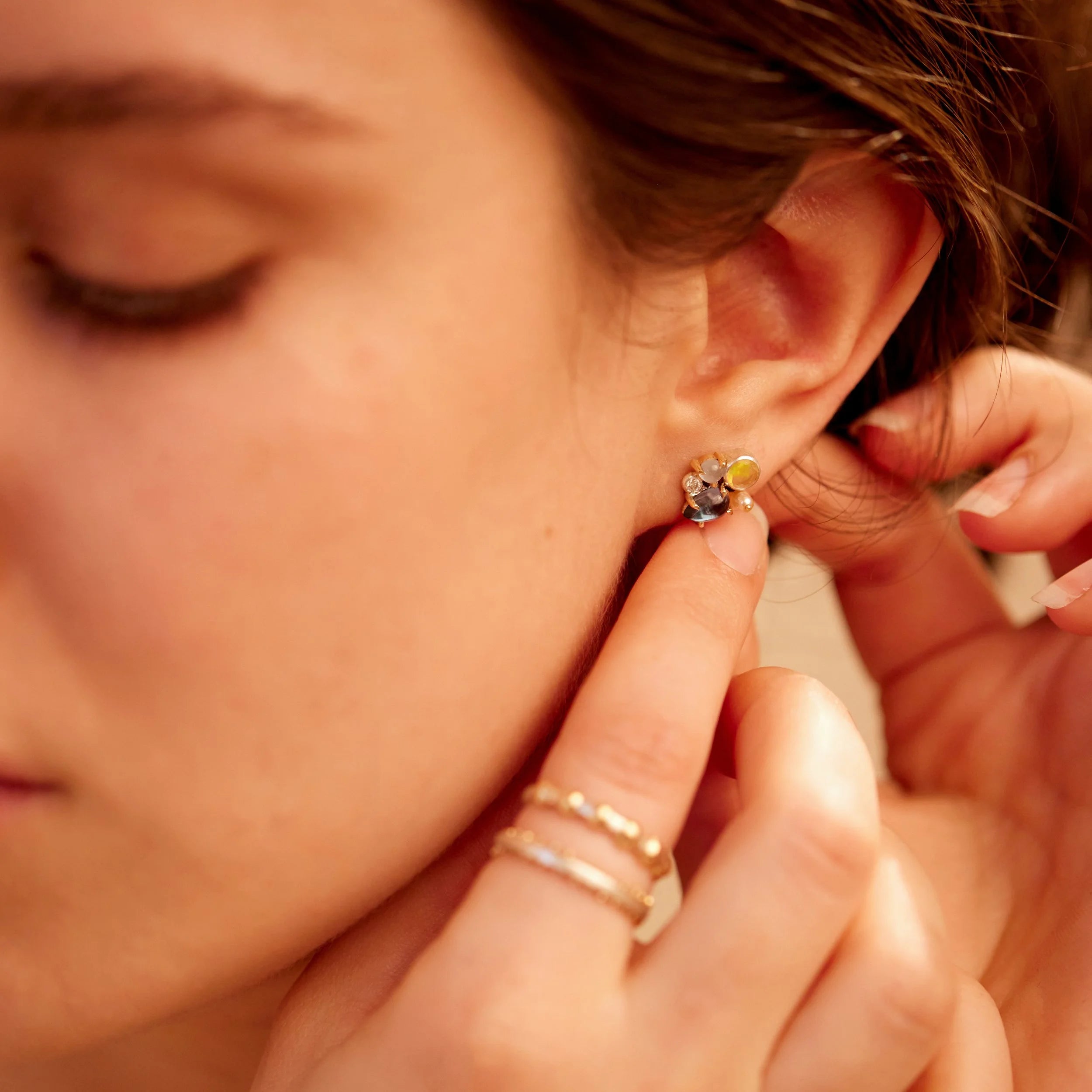 Close-up of a person wearing a gold earring with a gemstone.