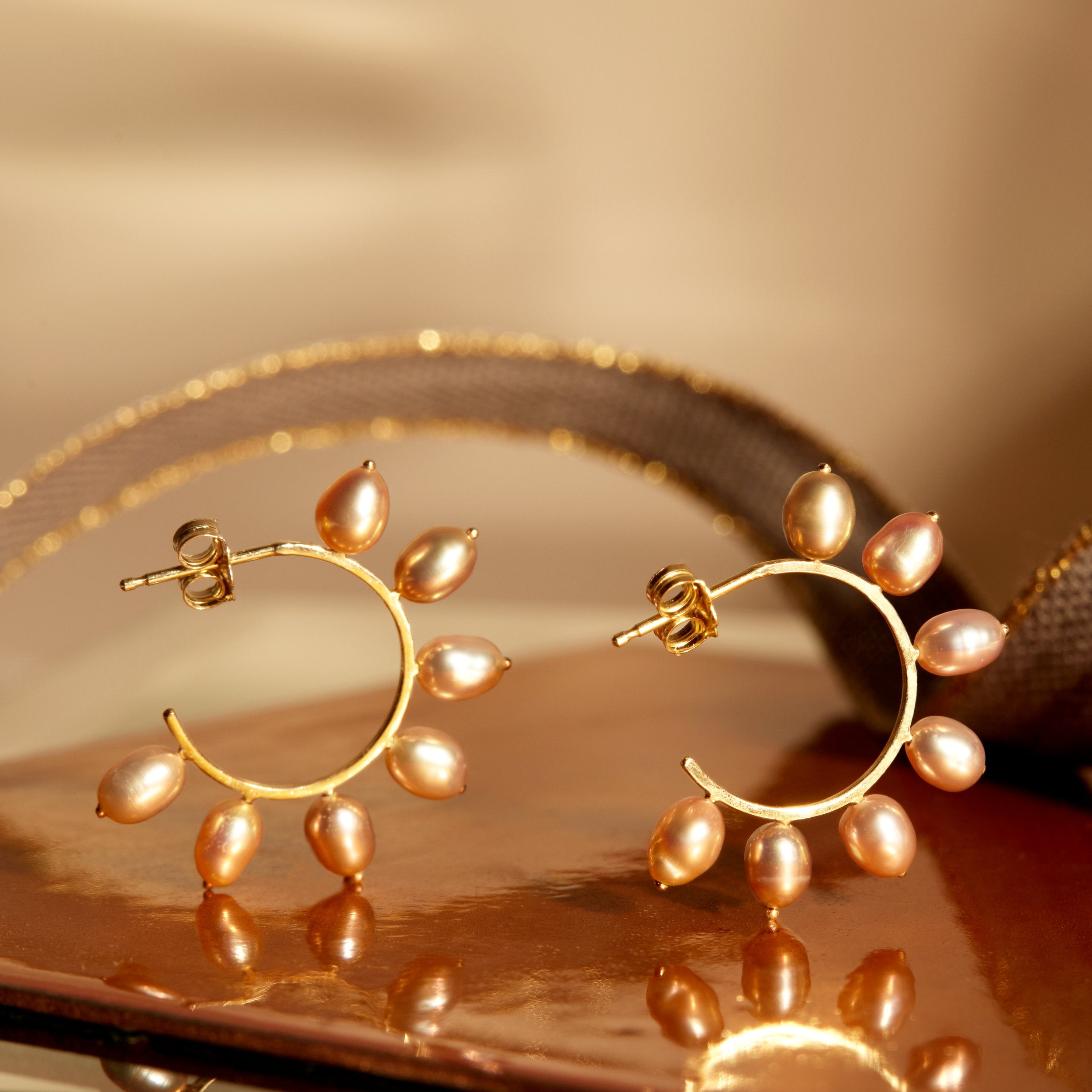 Gold hoop earrings with pearl beads on a reflective surface