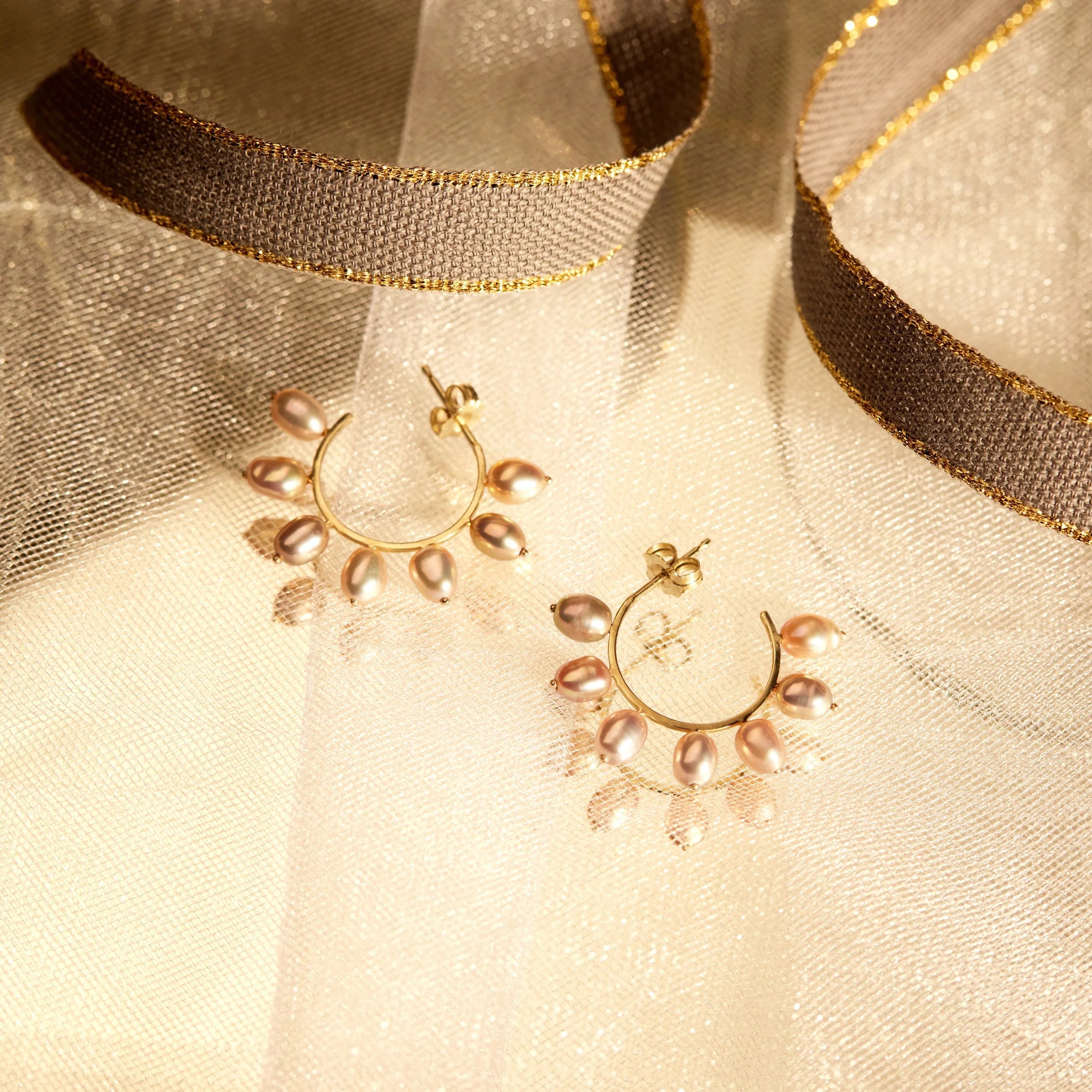 Gold hoop earrings with pearl beads on a soft fabric background