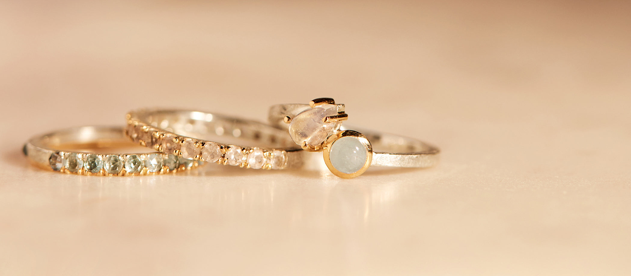 Three gold rings with gemstones on a beige background