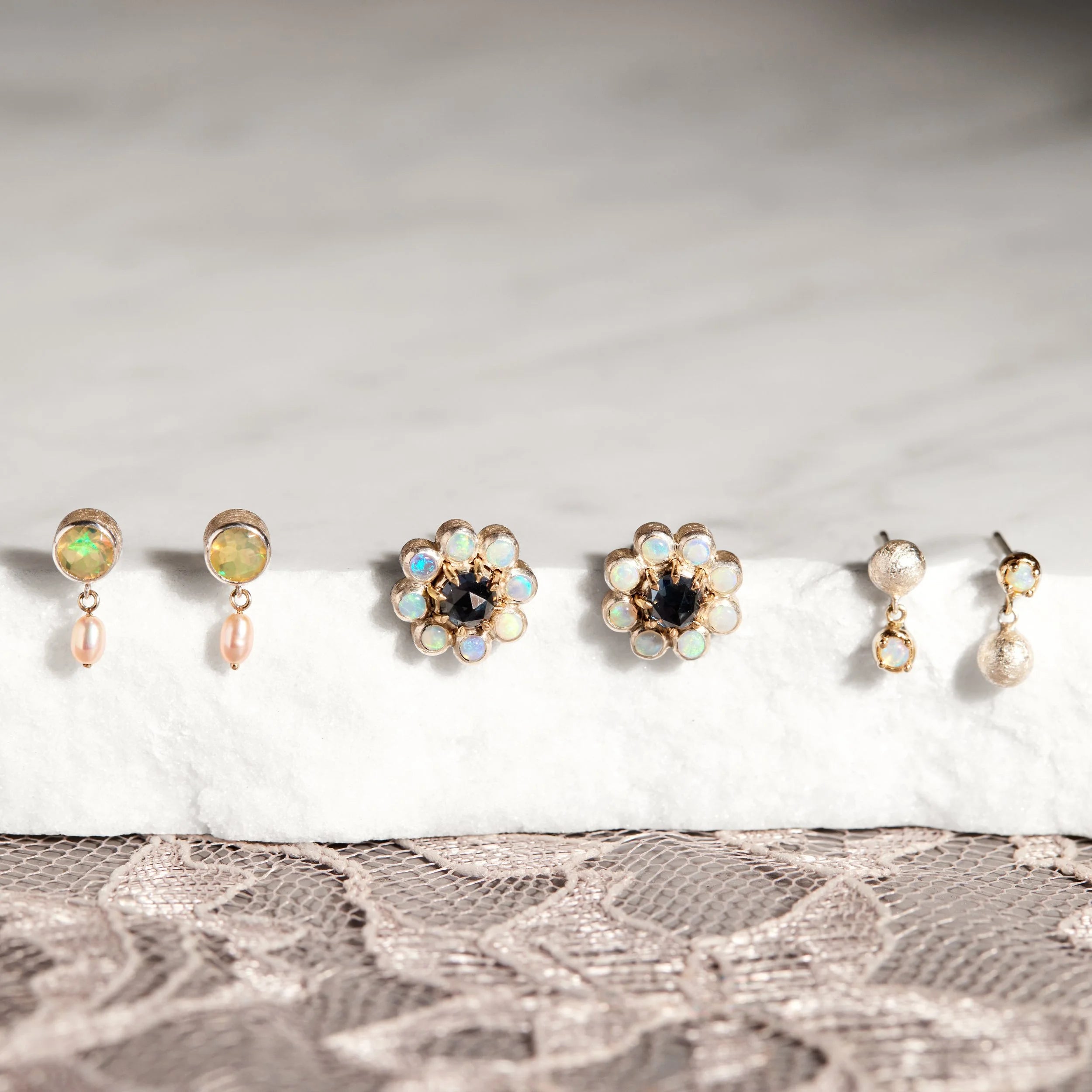 Set of earrings displayed on a white surface with a lace fabric background