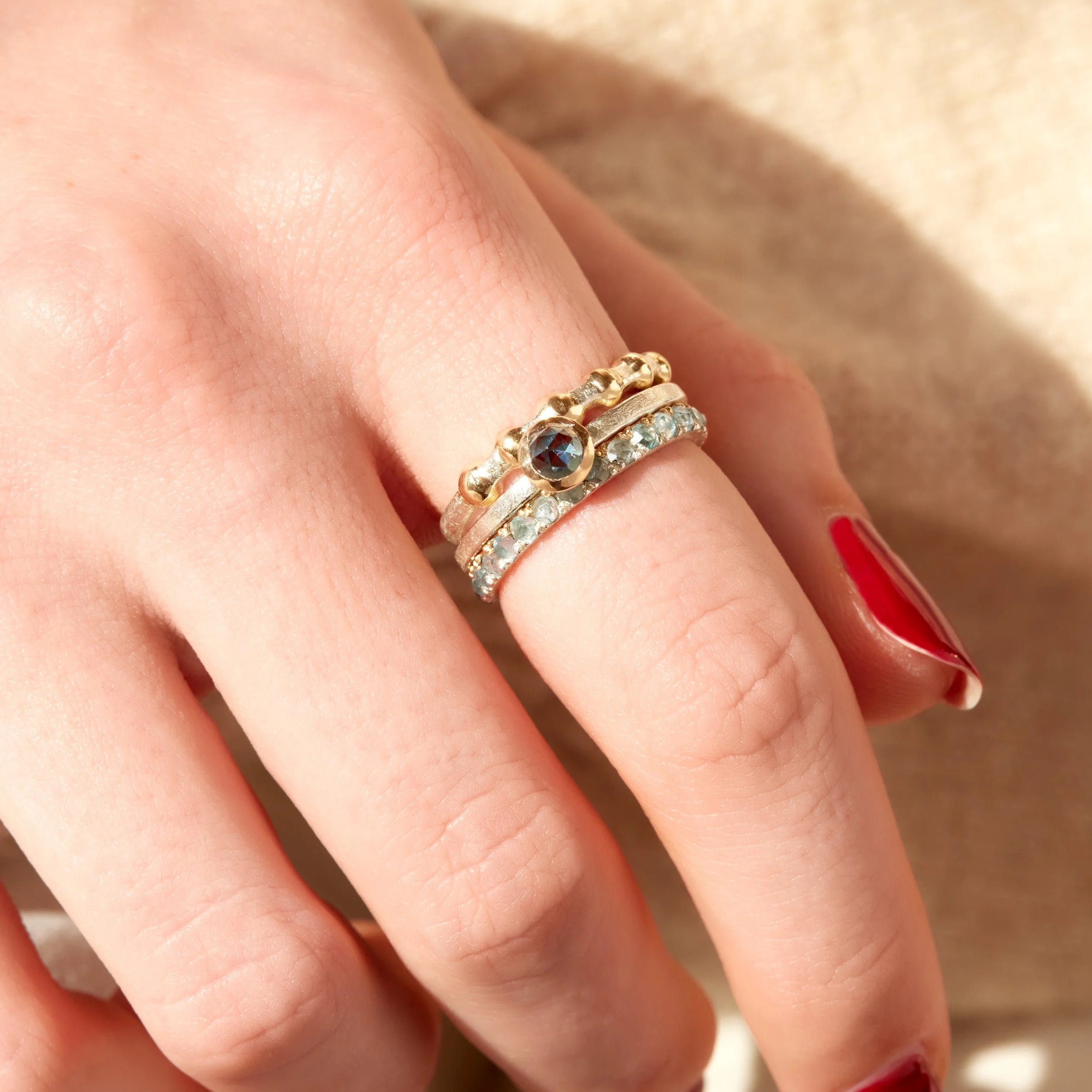 Close-up of a hand wearing three gold rings with gemstones on a neutral background