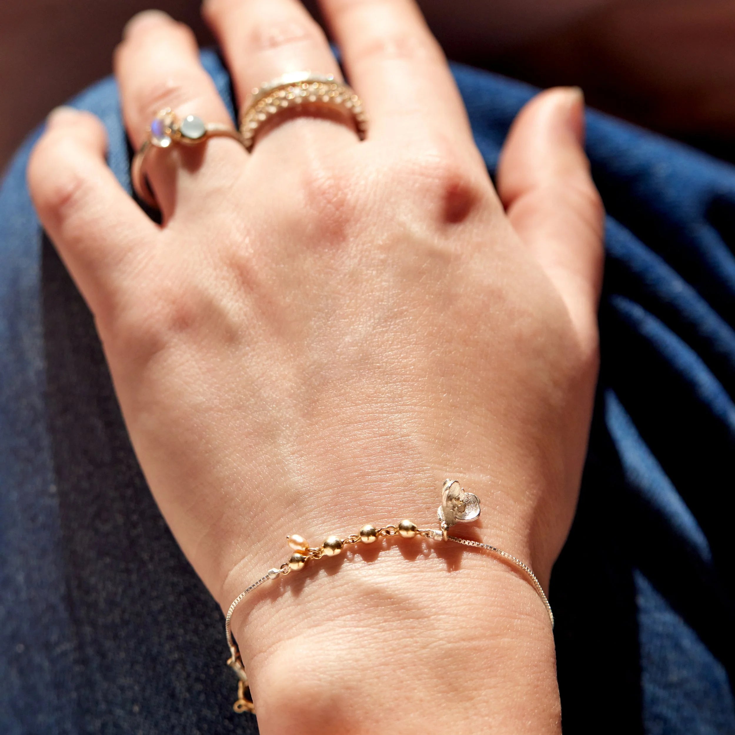 Hand wearing a gold bracelet and ring on a blue fabric background