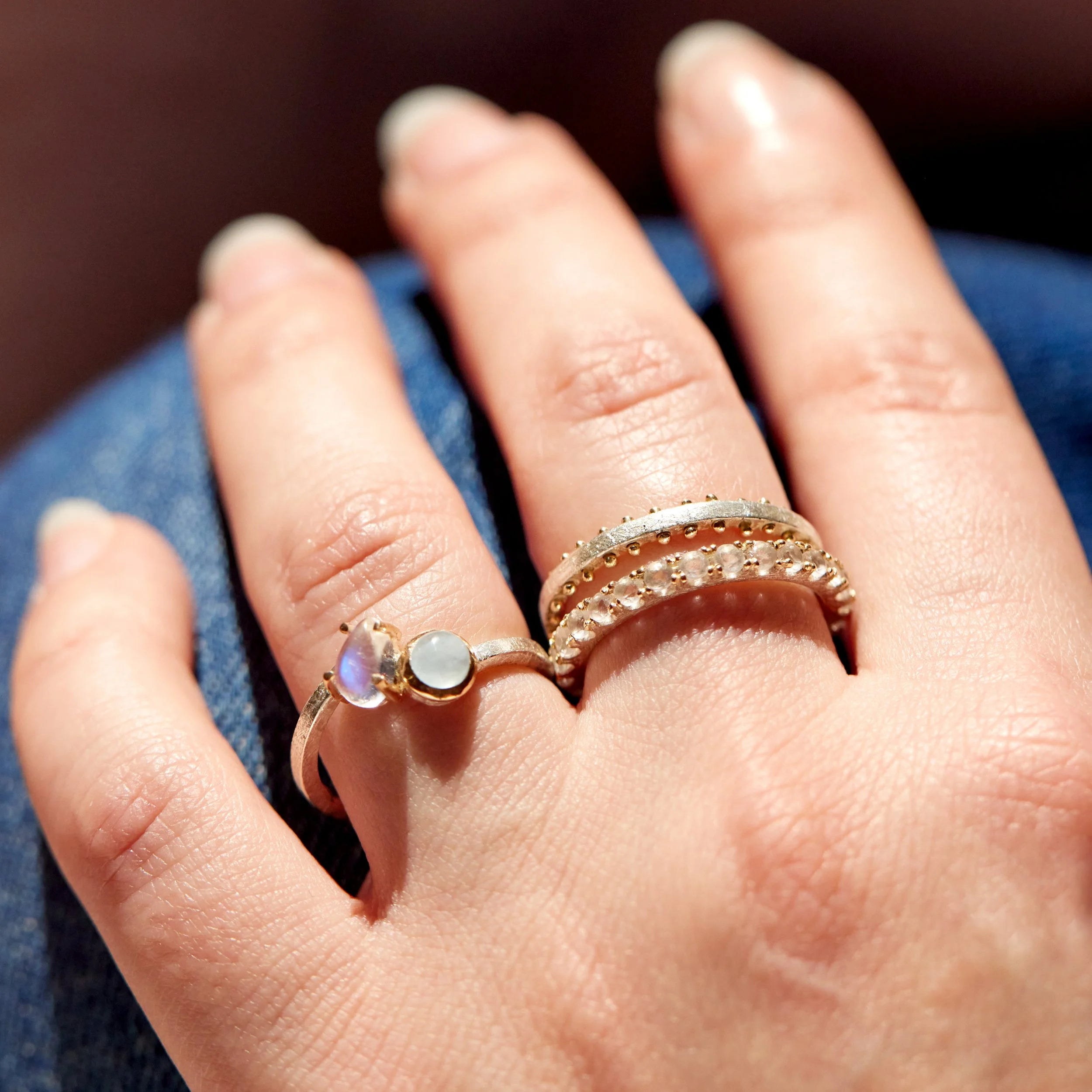 Close-up of a hand wearing two gold rings with gemstones on a dark background