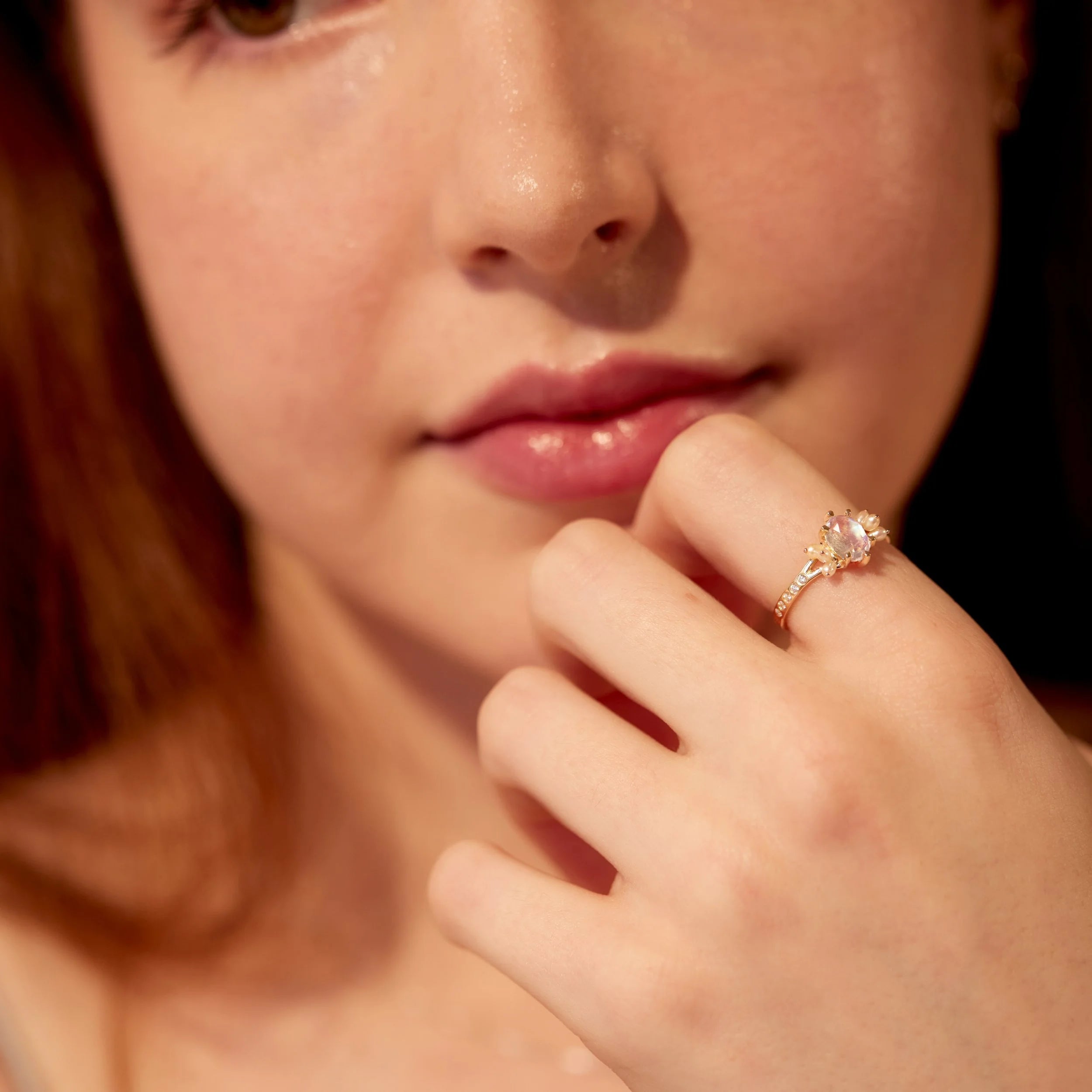 Close-up of a person wearing a ring with a pink gemstone, holding their chin.