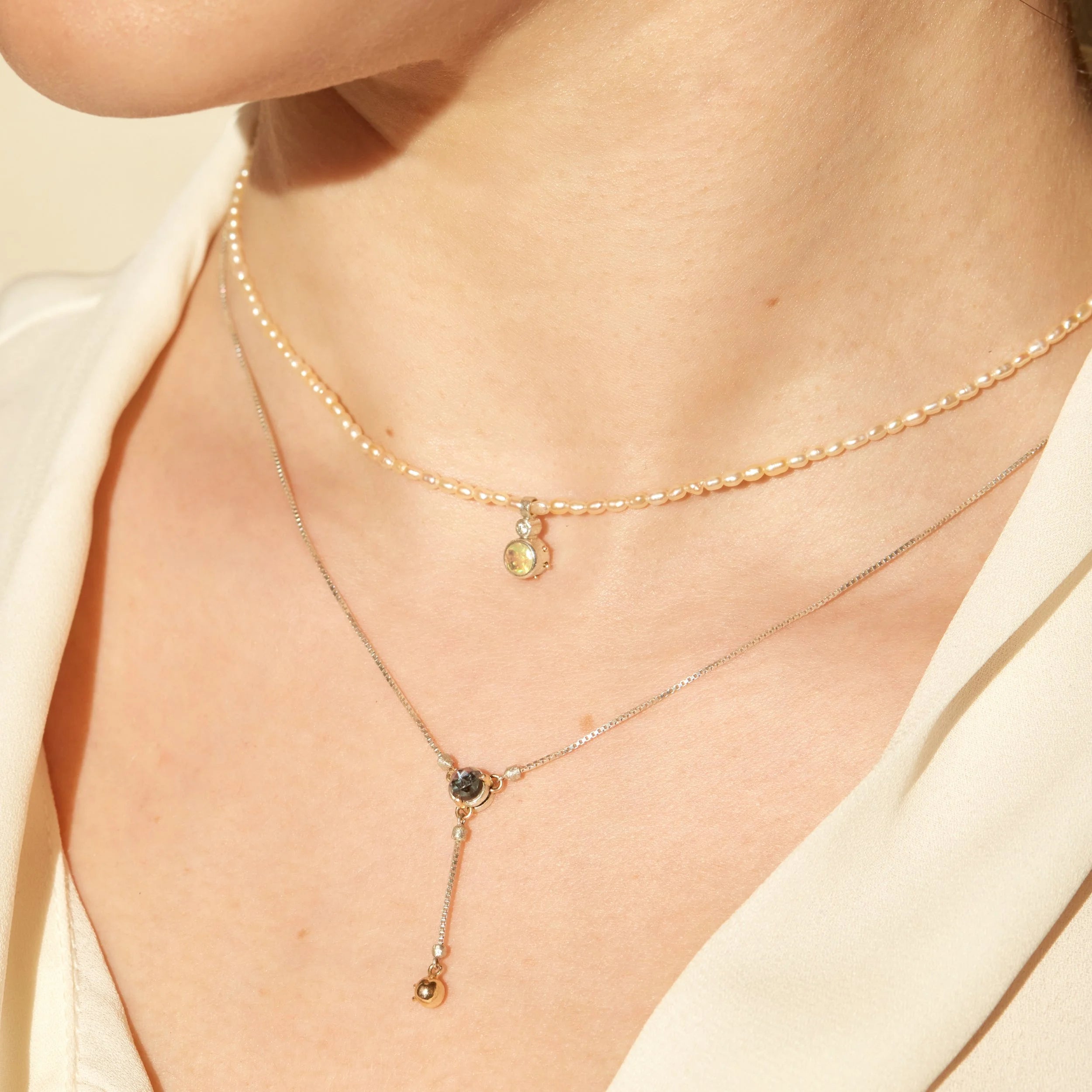 Close-up of a person wearing two delicate necklaces with small pendants on a light background.