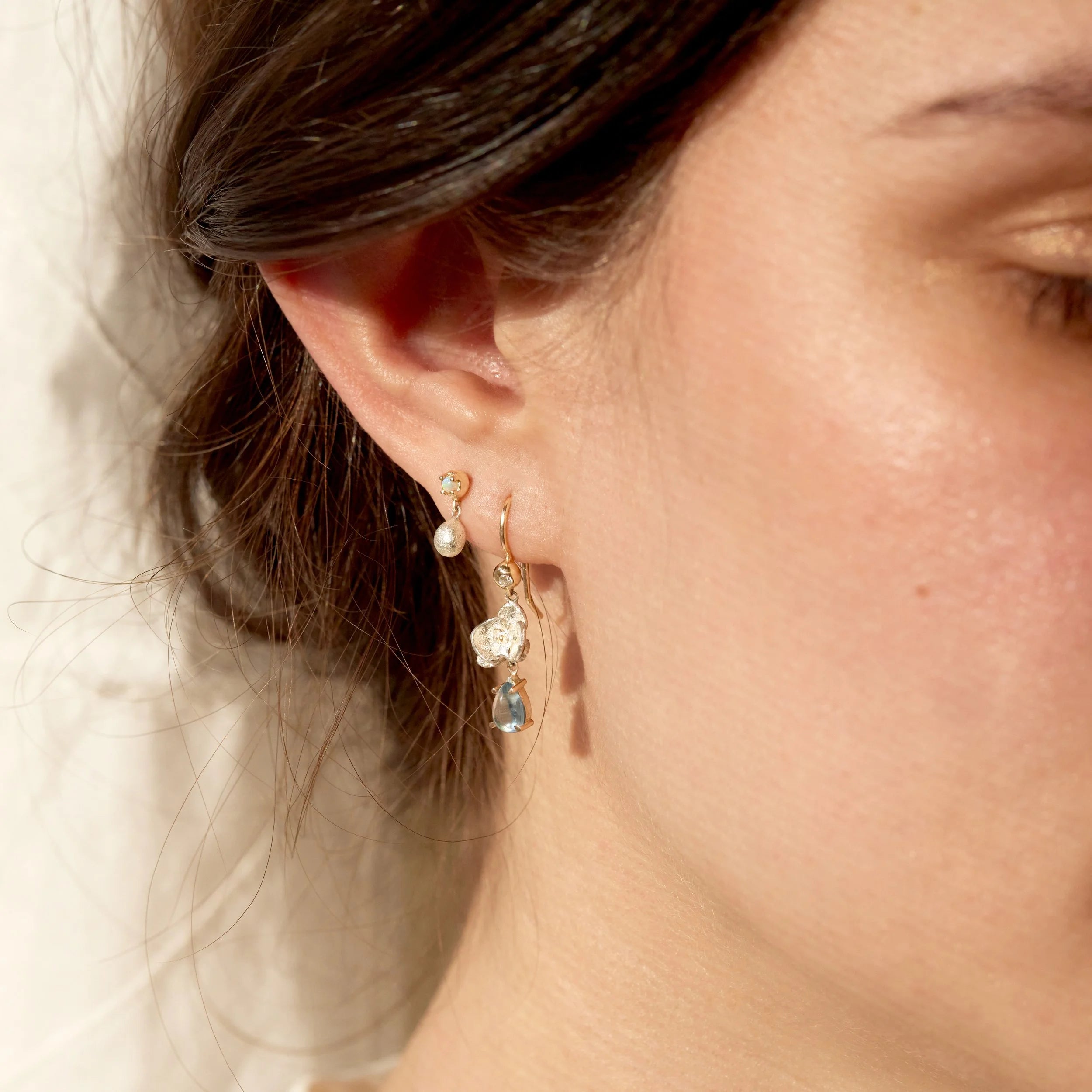 Close-up of a person wearing a gold earring with a teardrop-shaped gemstone.