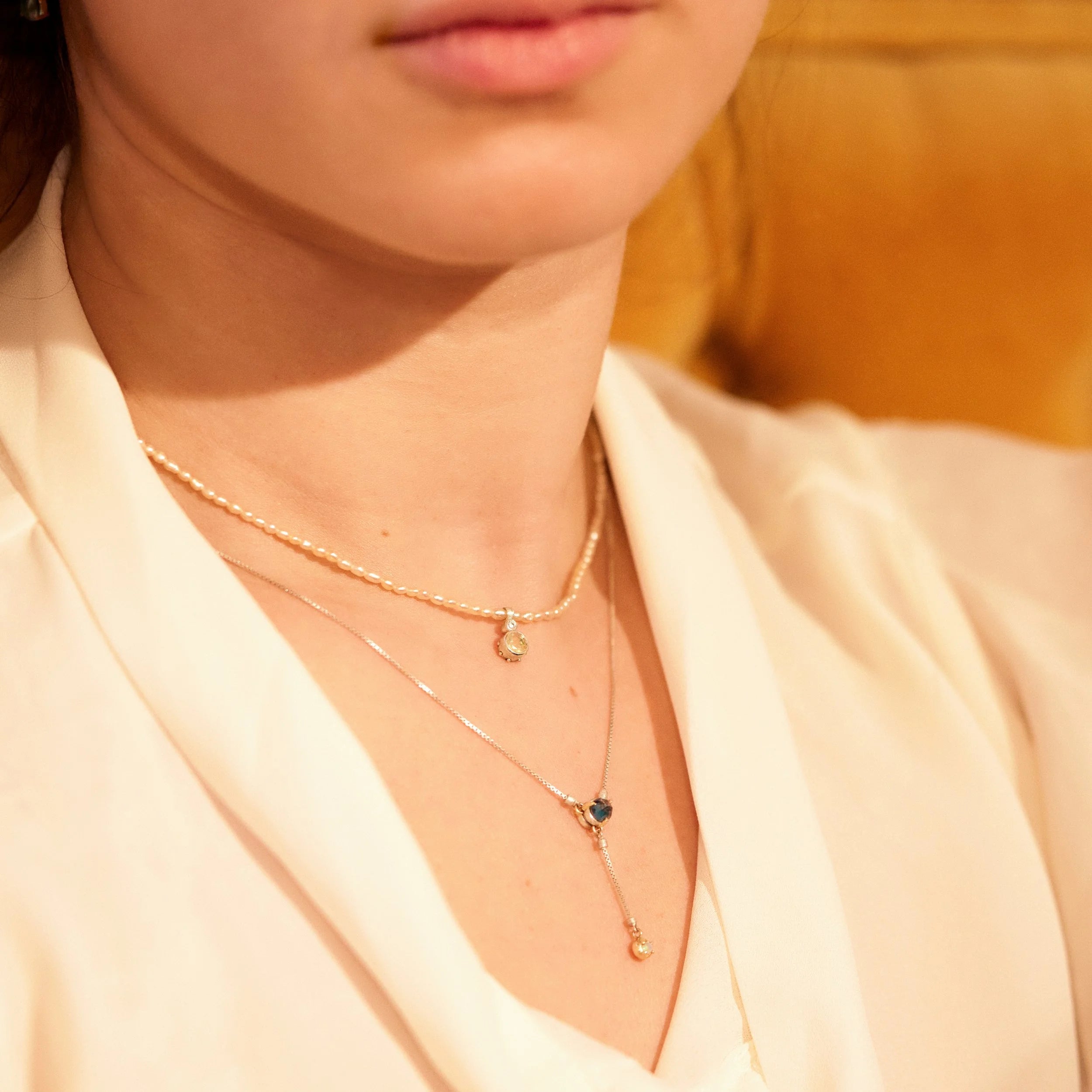 Close-up of a person wearing two gold necklaces with small pendants.