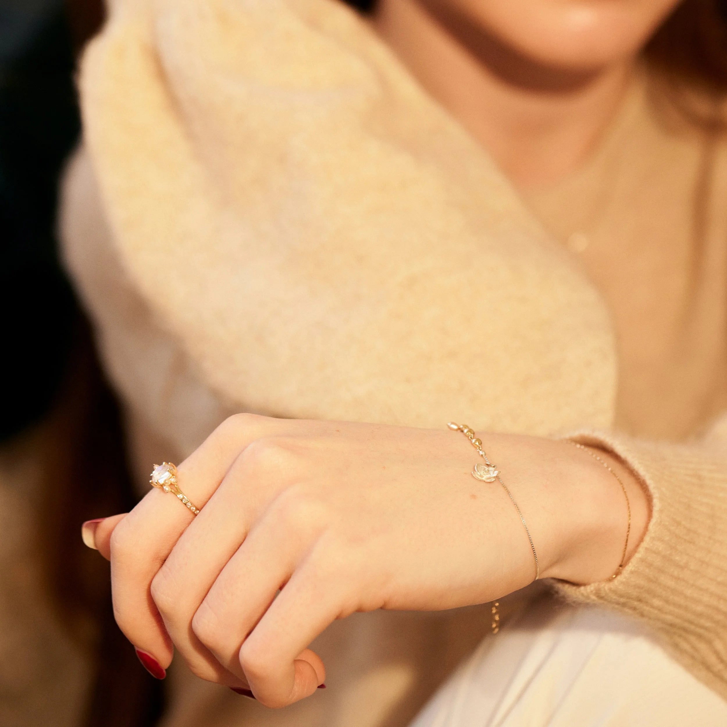 Close-up of a person's hand wearing gold rings and a bracelet against a blurred background.