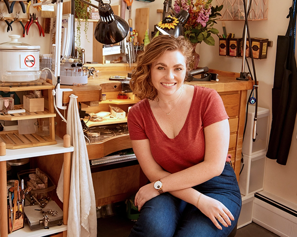 Allison sitting in a workshop or studio with tools and equipment around her