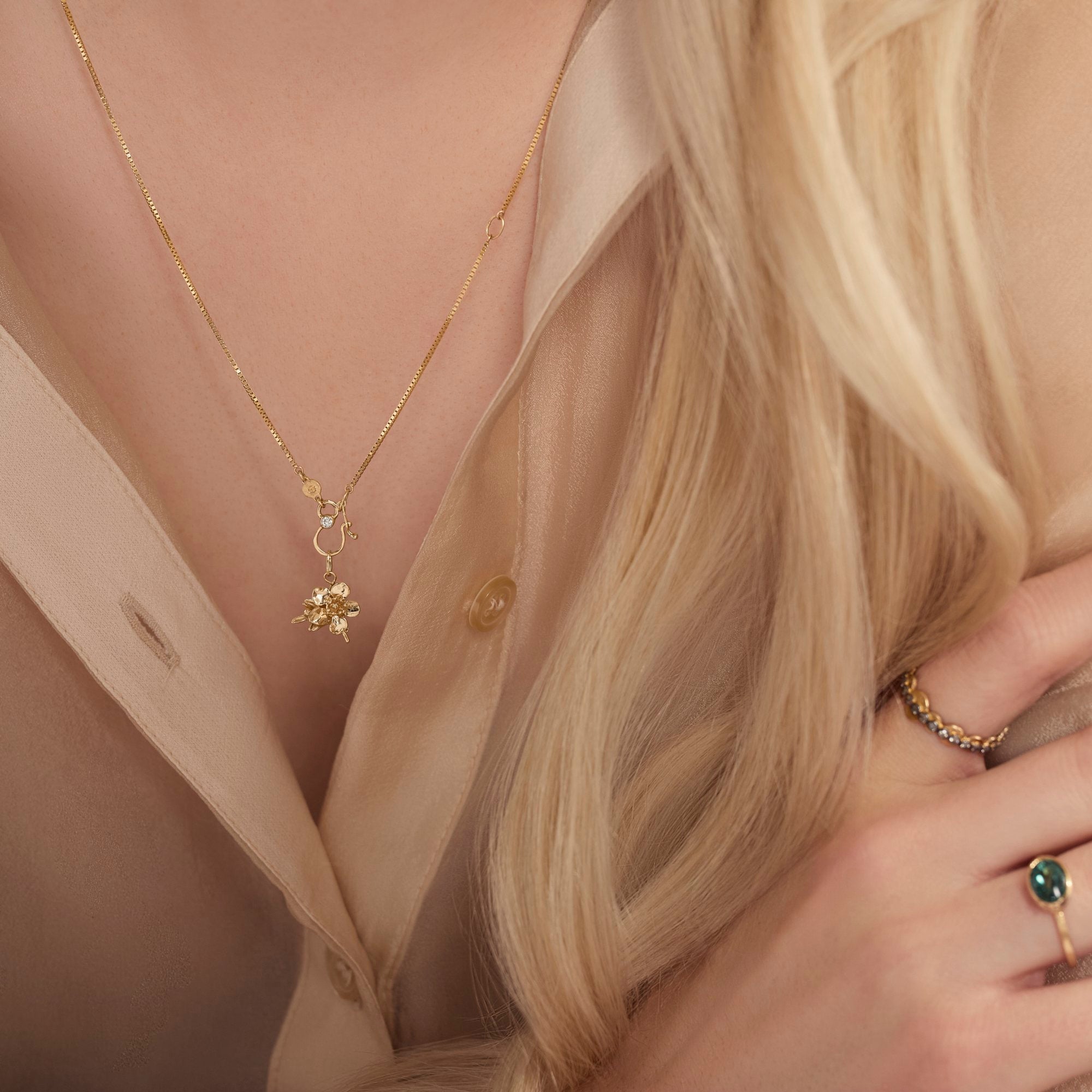 Close-up of a person wearing a gold necklace with a pendant, a ring, and a bracelet.