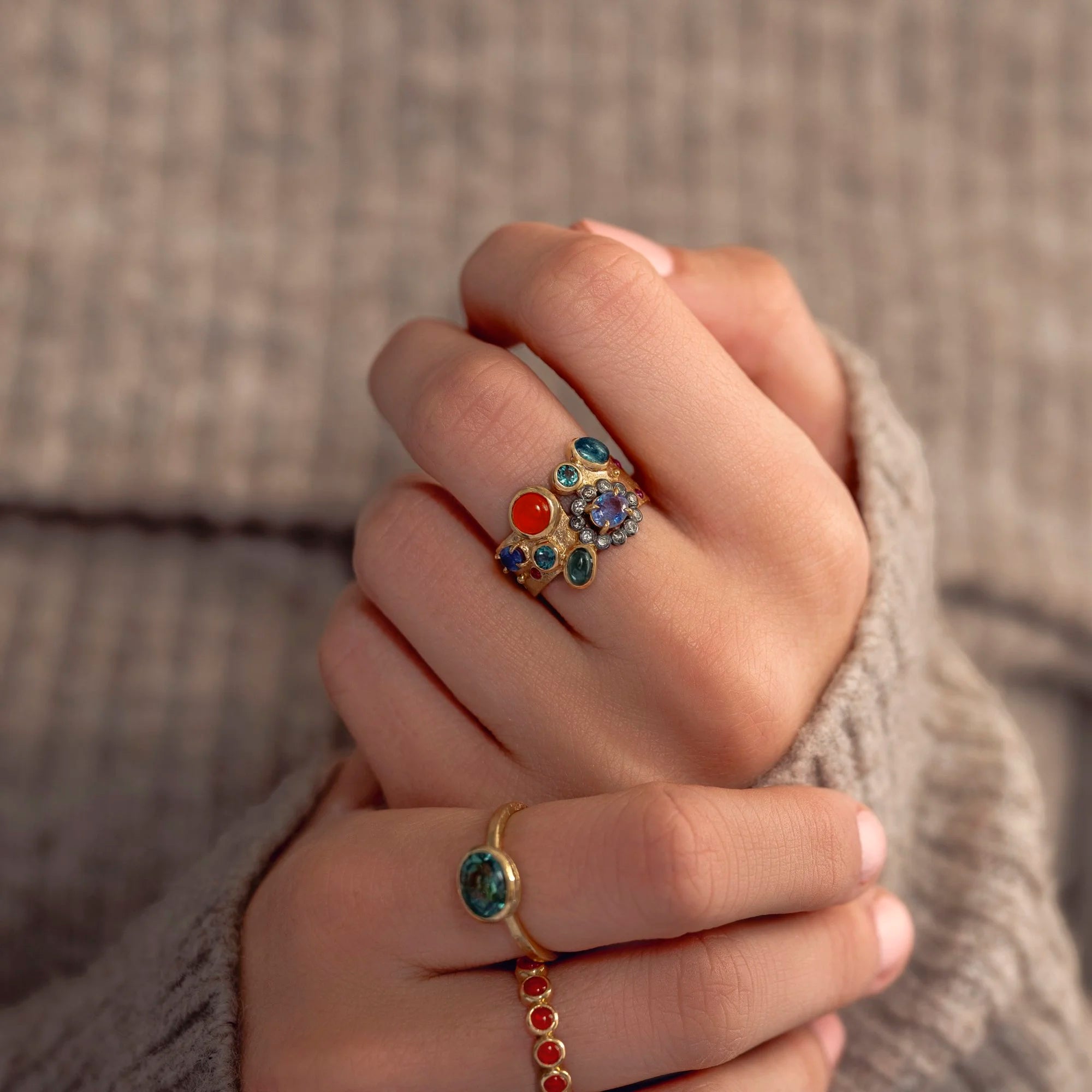 Close-up of a hand wearing three rings with colorful gemstones against a neutral background