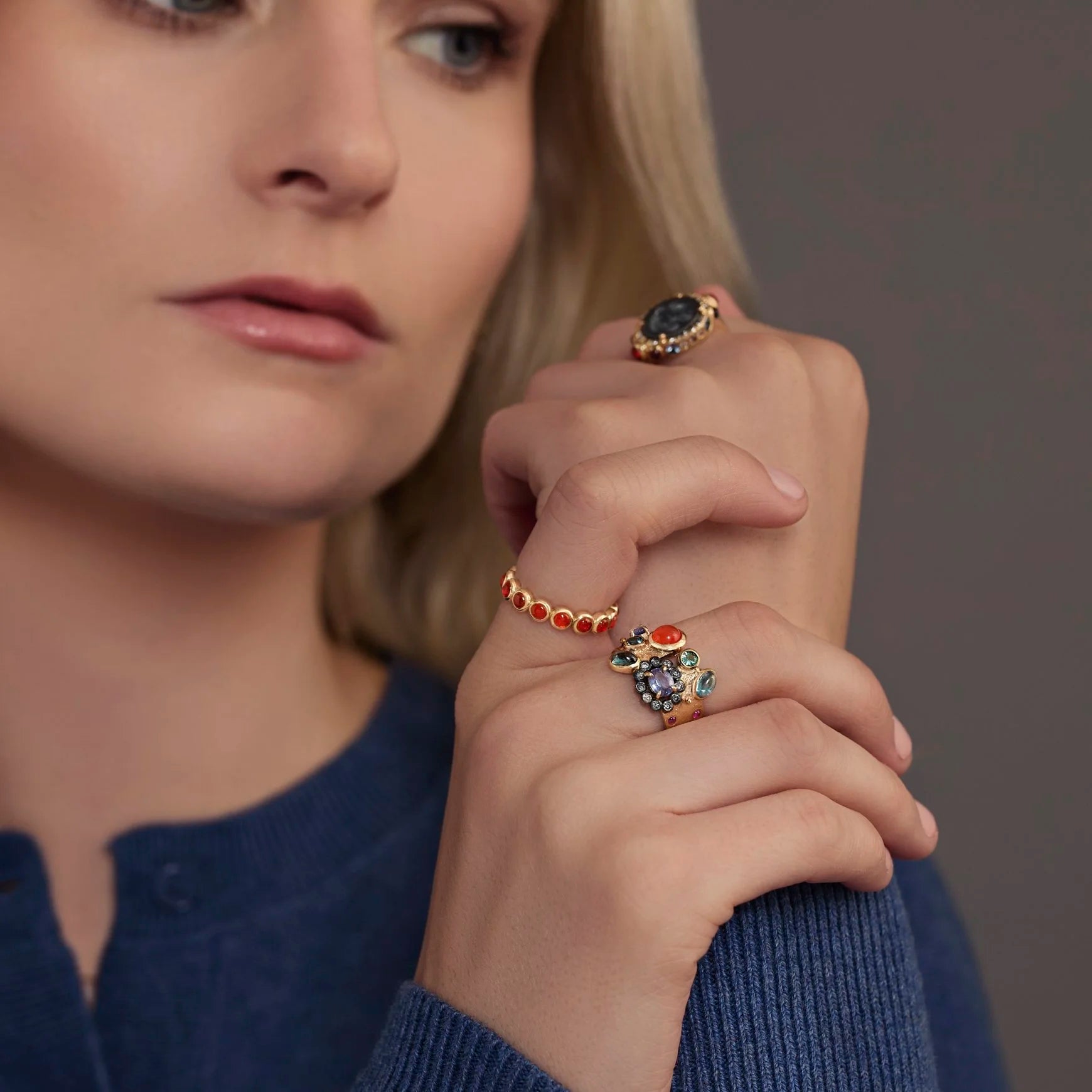 Woman wearing multiple rings with colorful gemstones on a neutral background