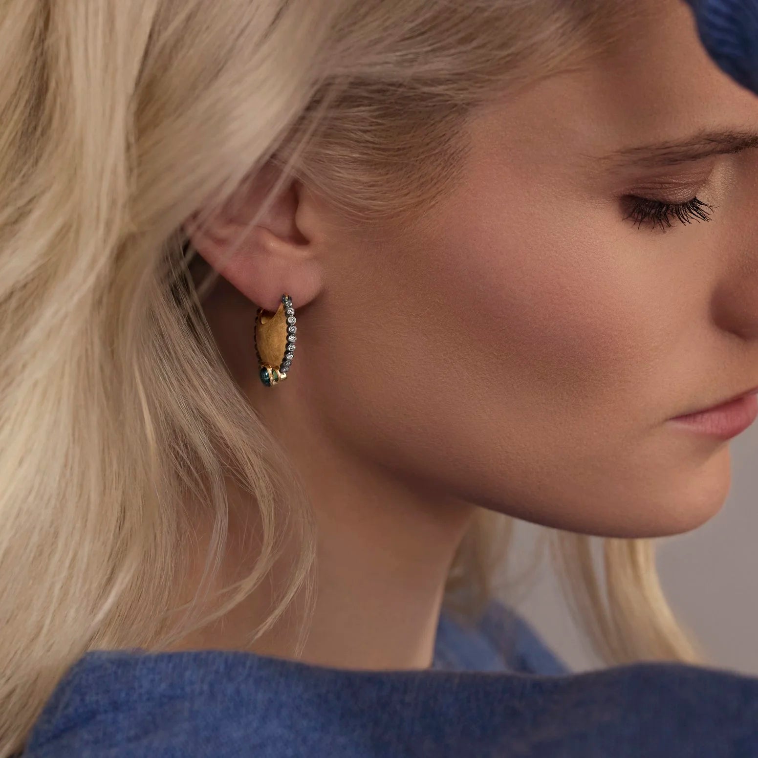 Close-up of a woman wearing a hoop earring with a blue and diamond gemstone.