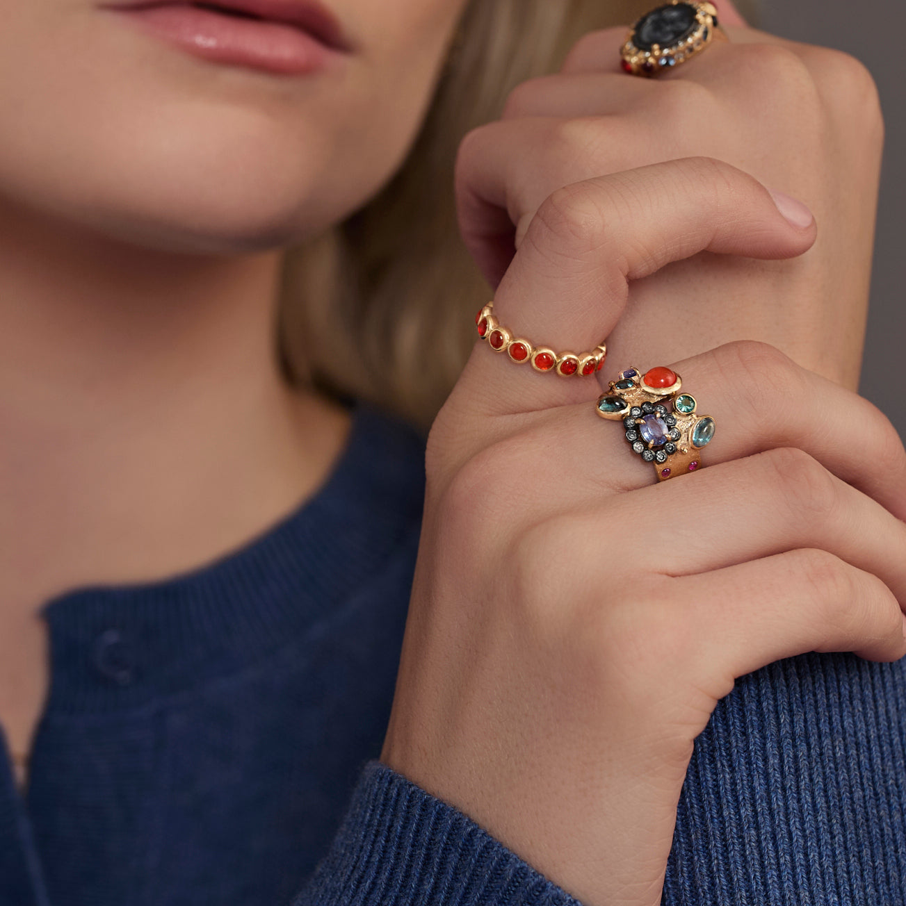 Close-up of a person wearing two rings with colorful gemstones on a neutral background