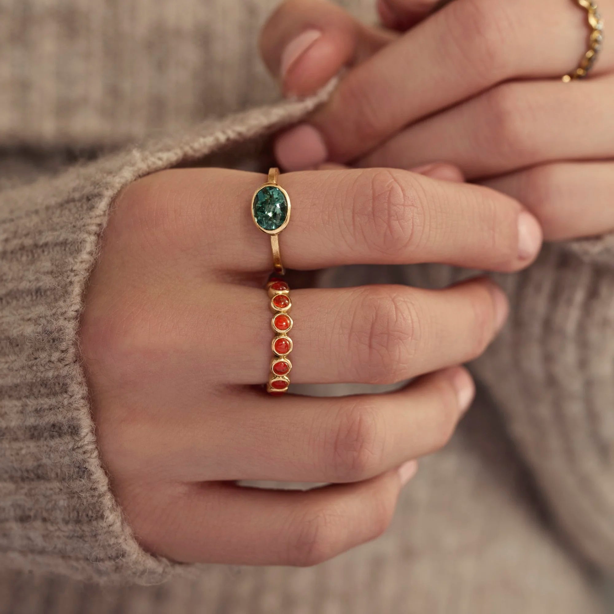 Close-up of a hand wearing two gold rings with gemstones.
