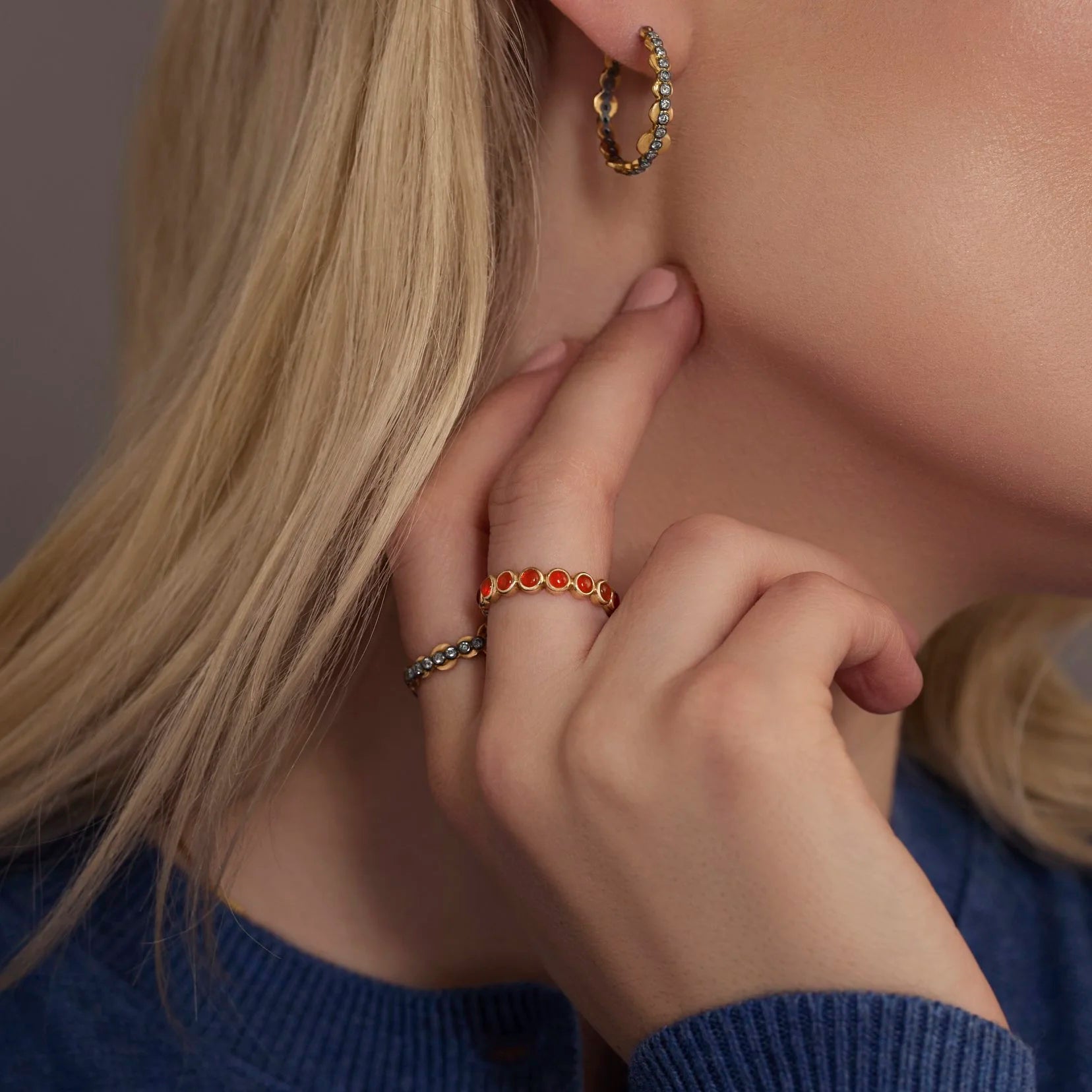Close-up of a person wearing gold hoop earrings, orange gemstone ring, and blue sweater.