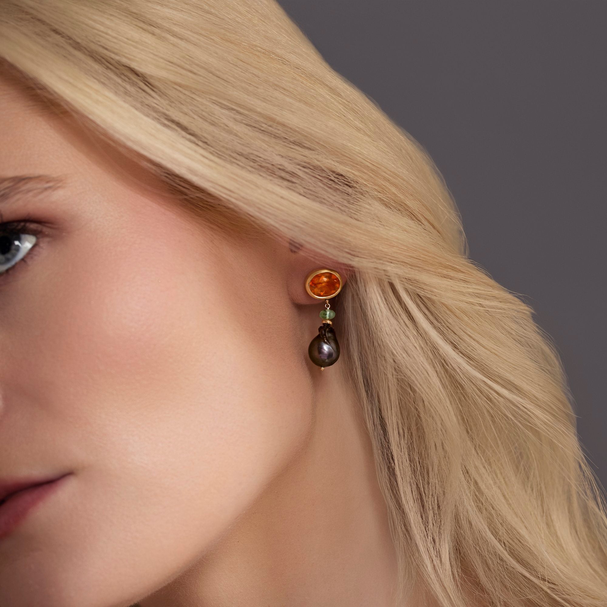 Close-up of a woman wearing an earring with a dark stone on a neutral background