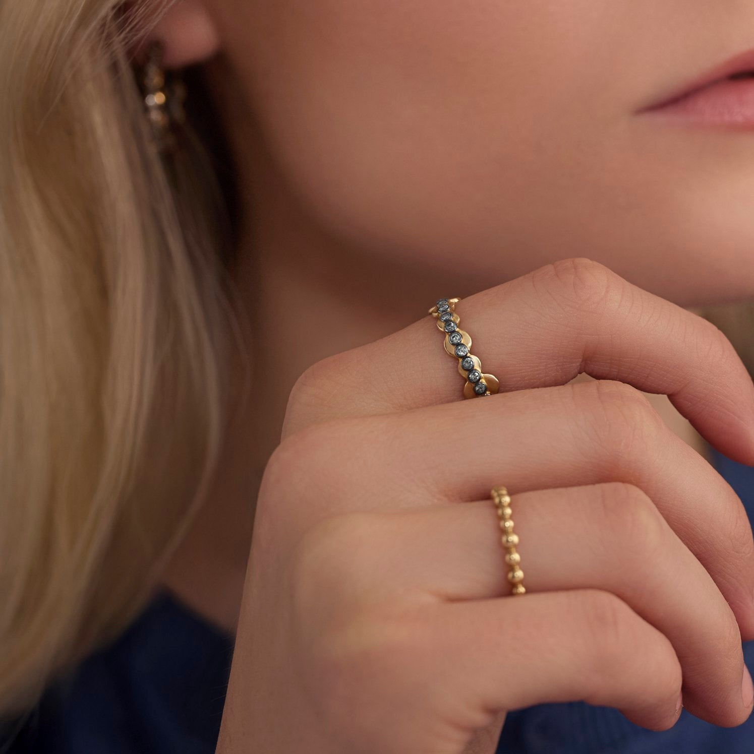 Close-up of a person's hand wearing two gold rings with small stones.