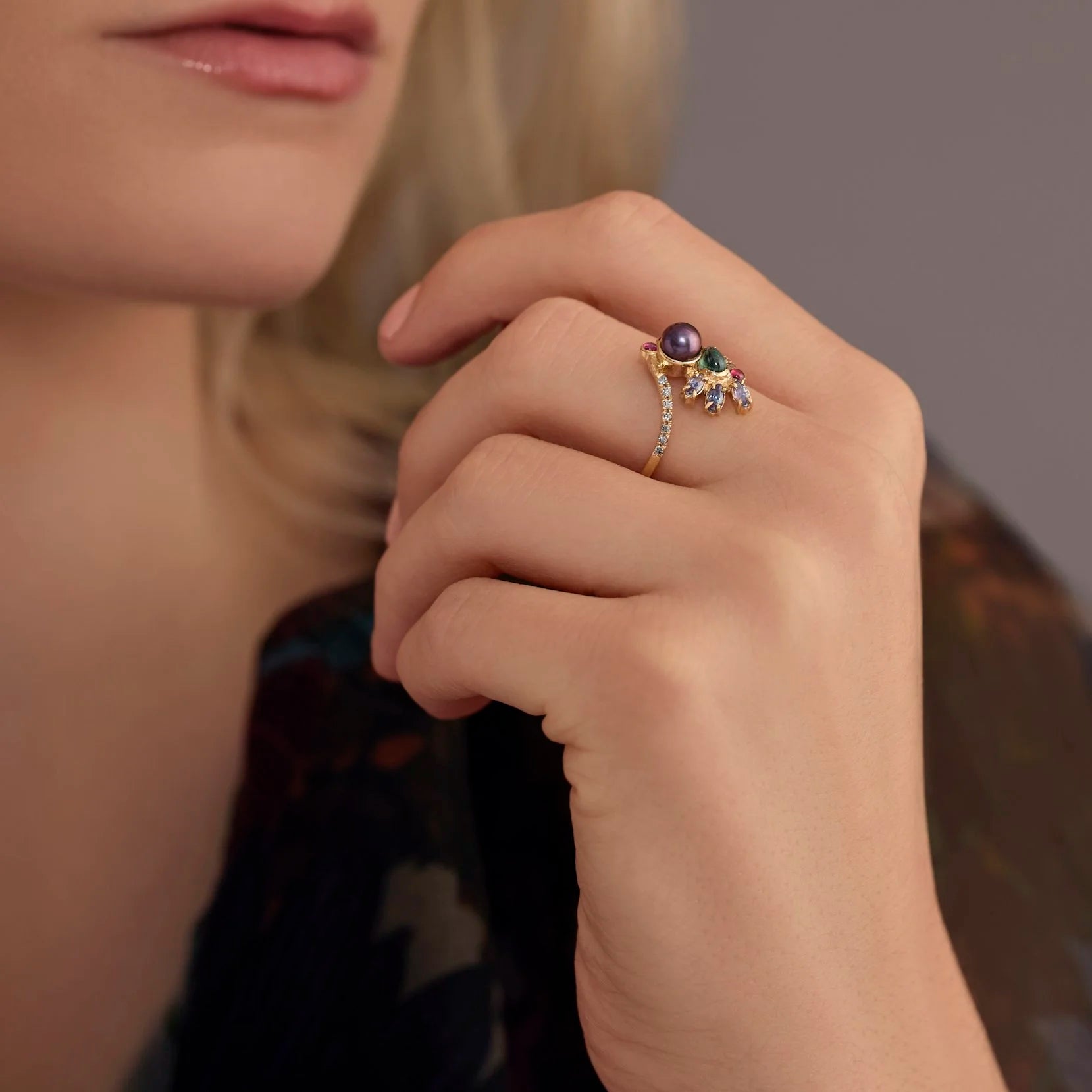 Close-up of a hand wearing a decorative ring with gemstones on a blurred background
