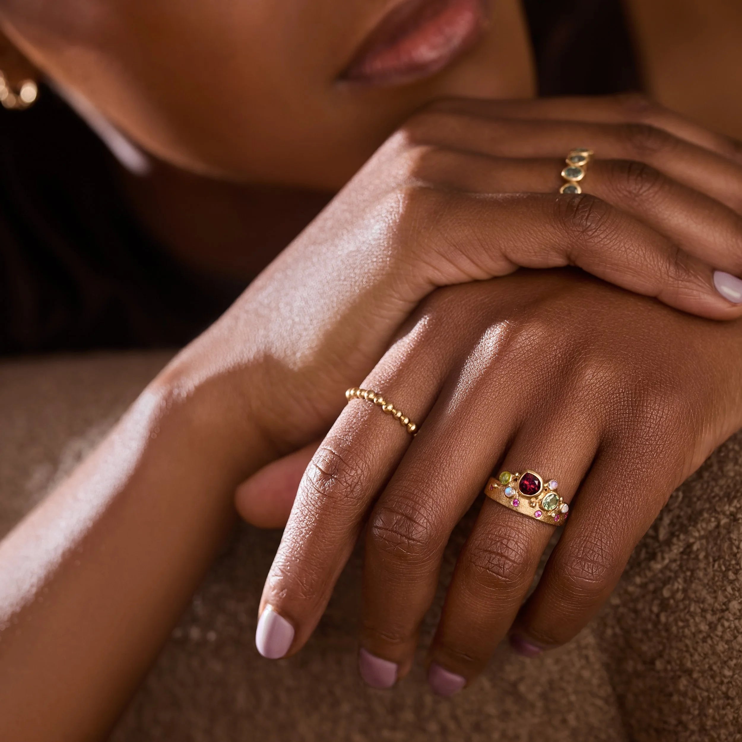 Close-up of a person's hands with gold rings on a neutral background