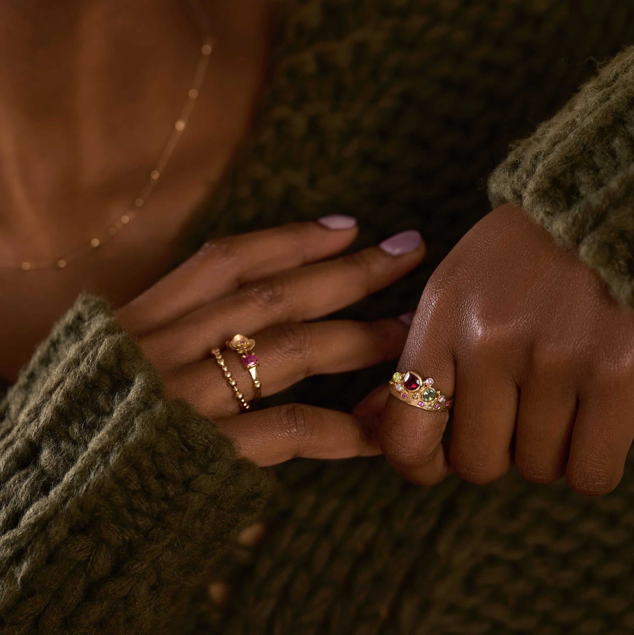 Close-up of two hands wearing gold rings with gemstones against a textured brown background.