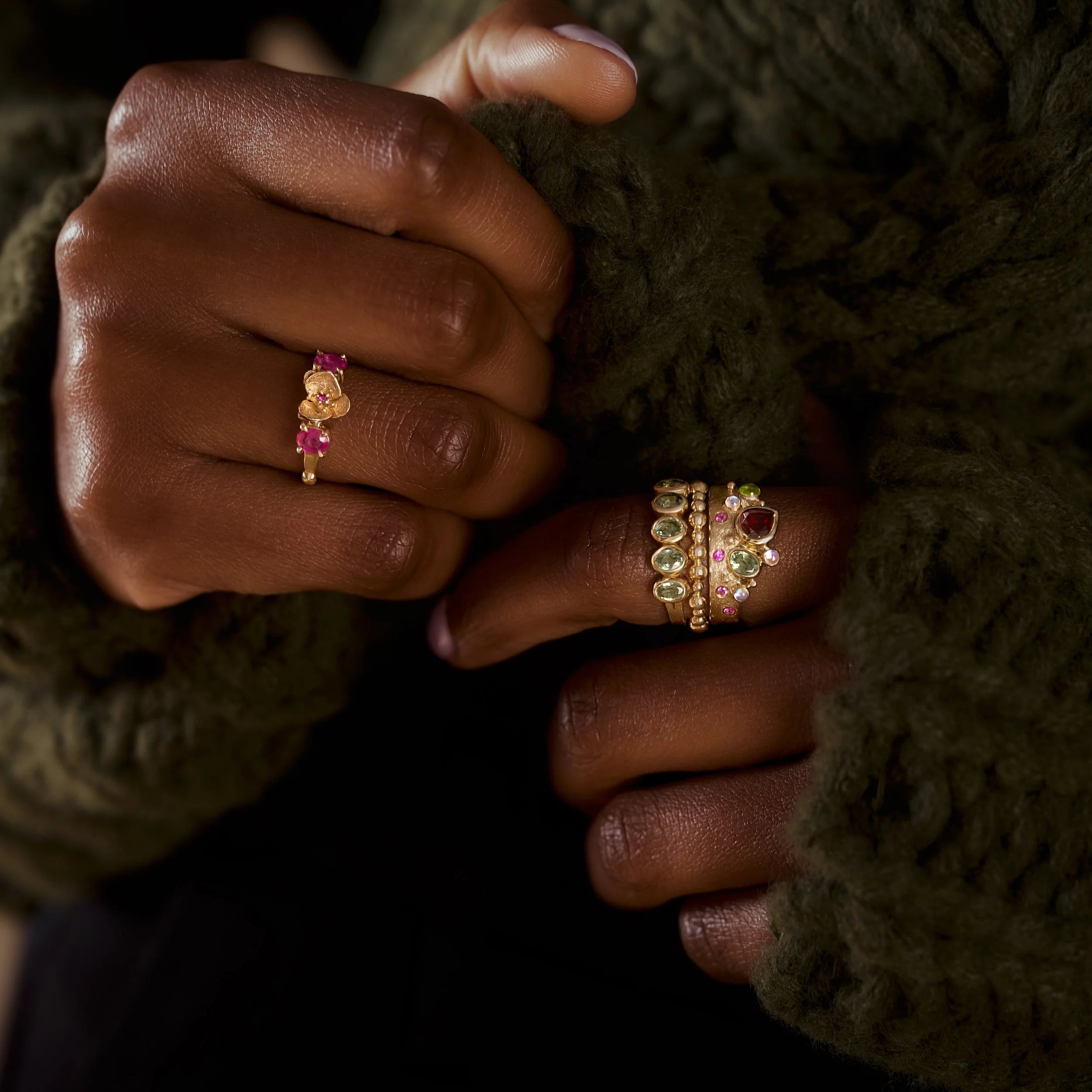 Close-up of a hand wearing three gold rings with gemstones against a dark background.