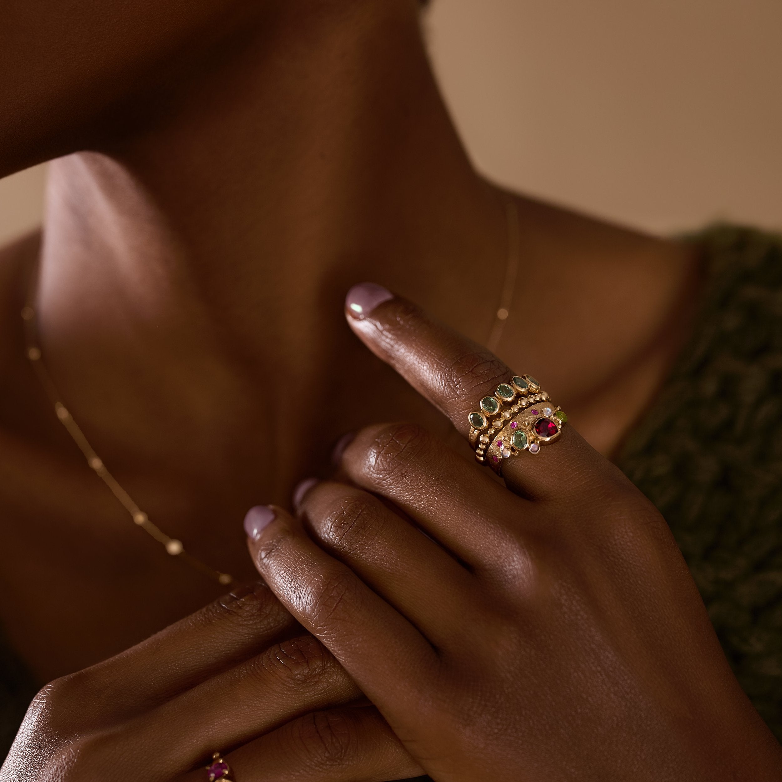 Close-up of a hand wearing a gold ring with gemstones against a neutral background