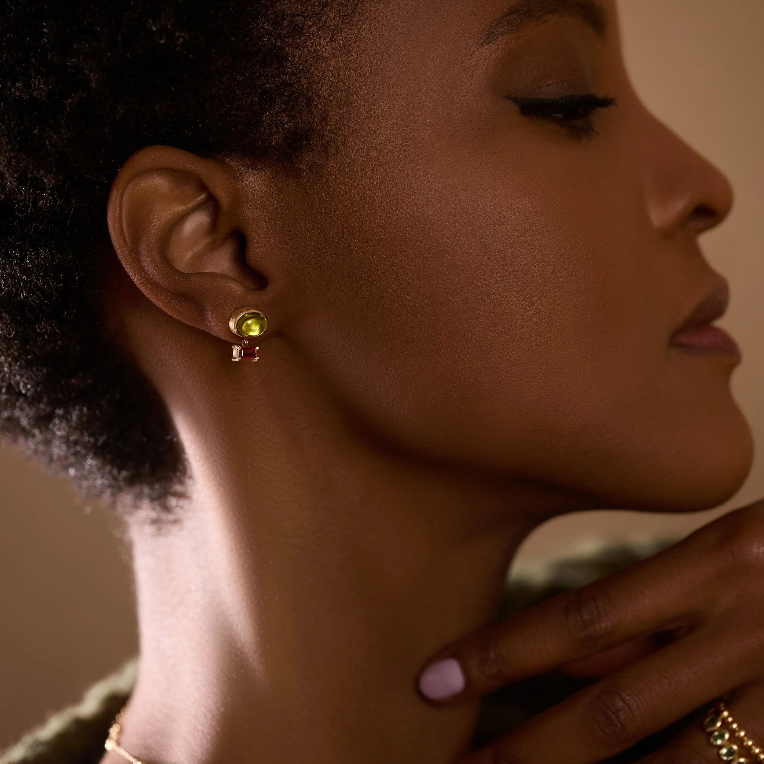 Close-up of a woman wearing a green gemstone earring with a neutral background