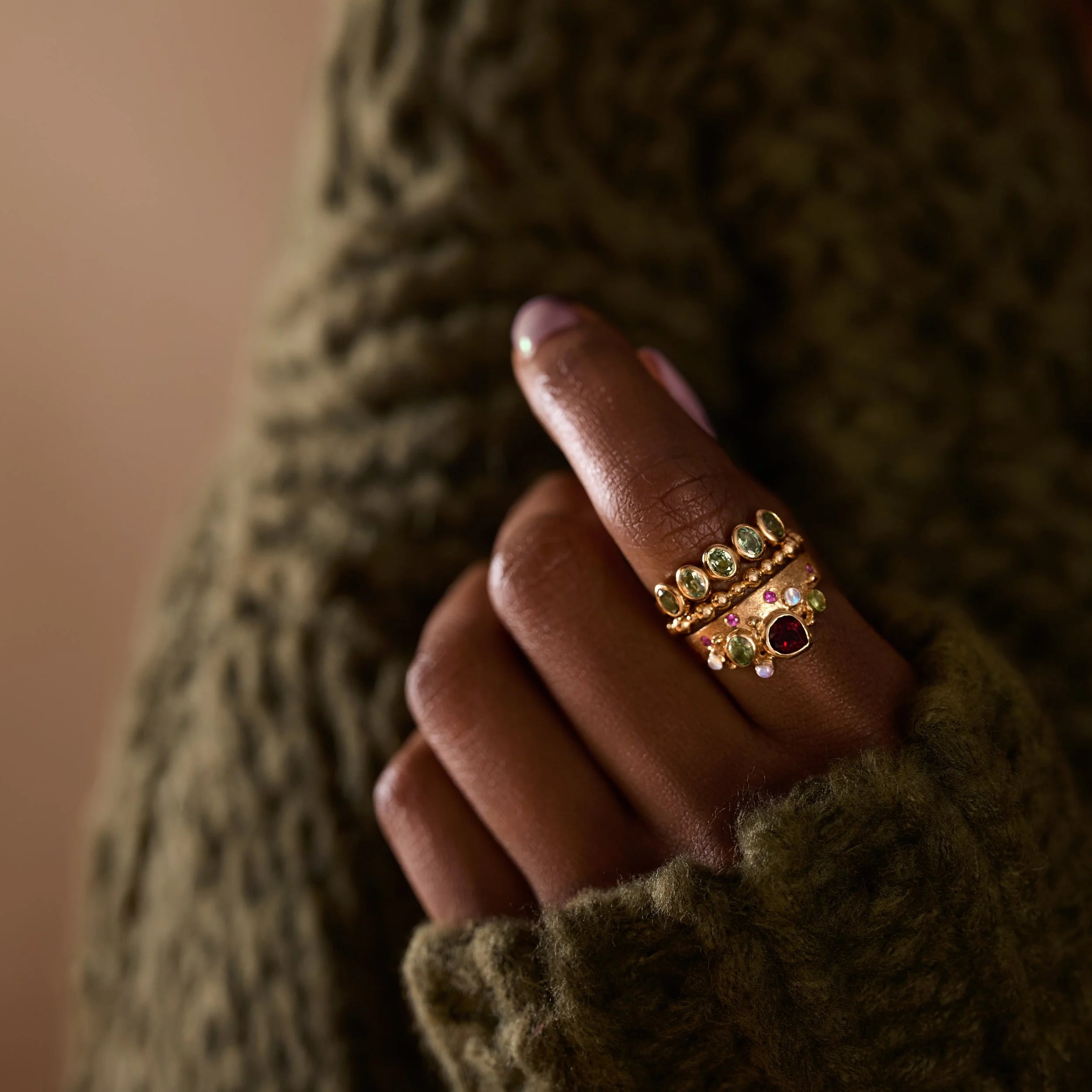 Hand wearing a gold ring with gemstones against a textured green background