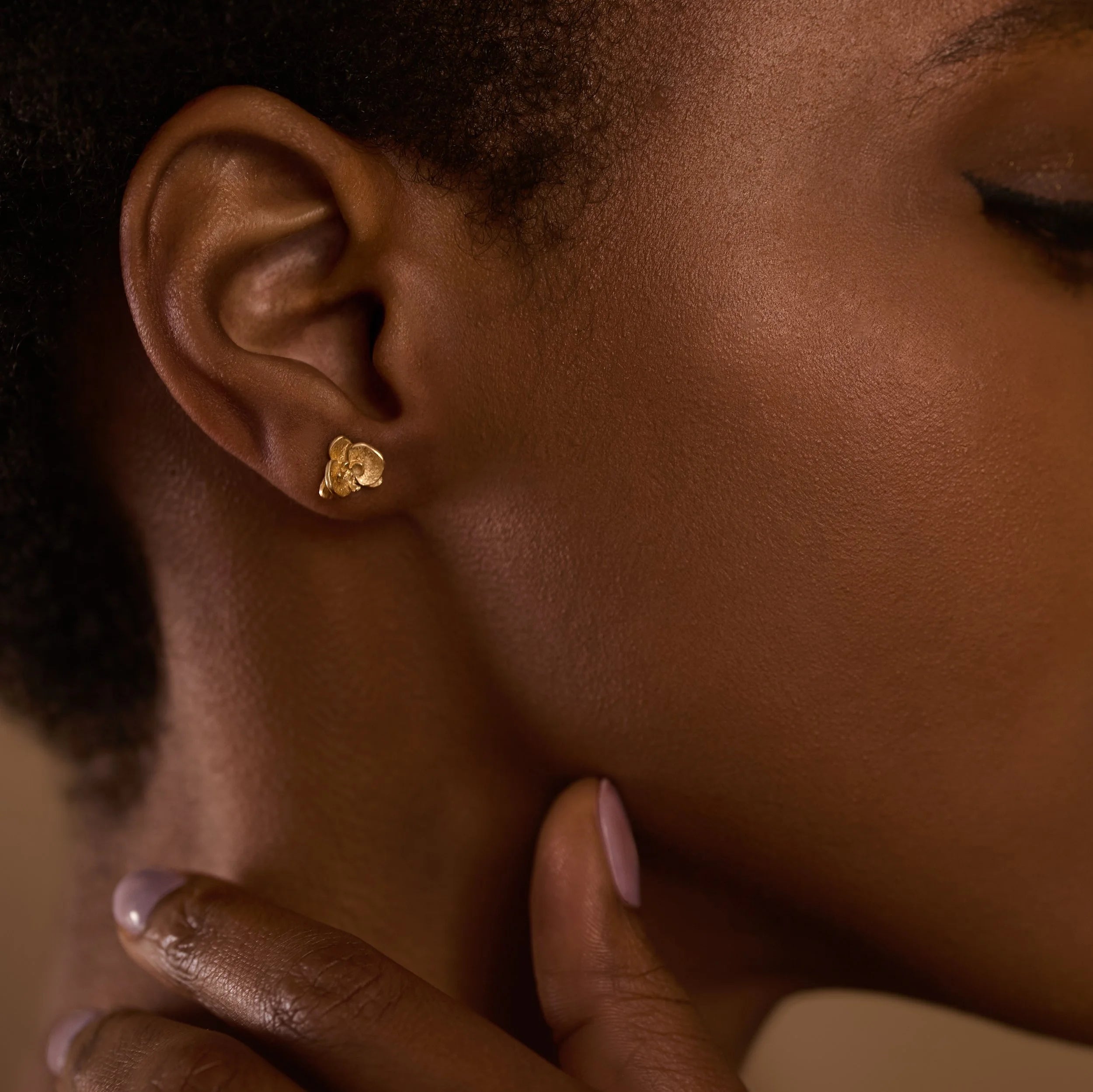 Close-up of an ear wearing a gold earring with a blurred background