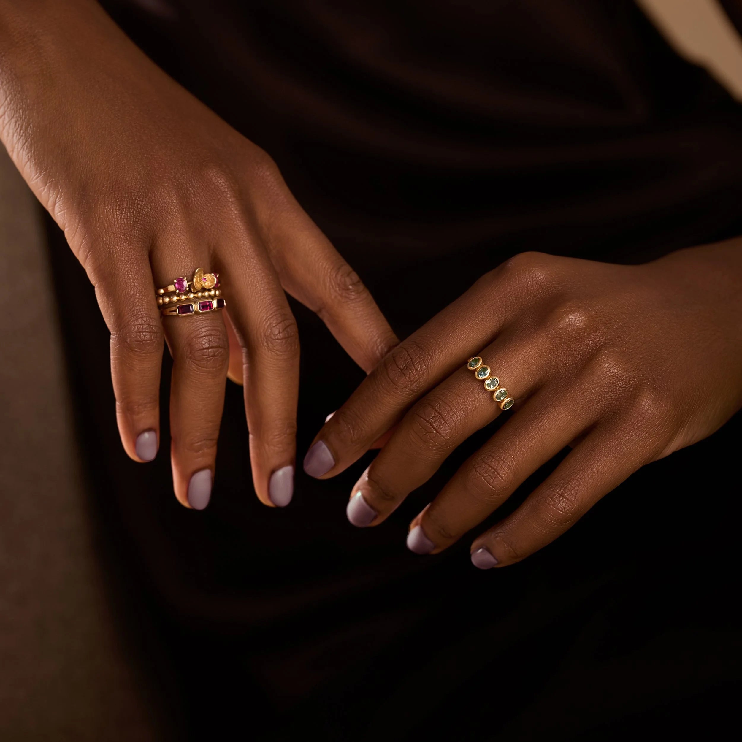 Close-up of two hands wearing gold rings with gemstones on a dark background