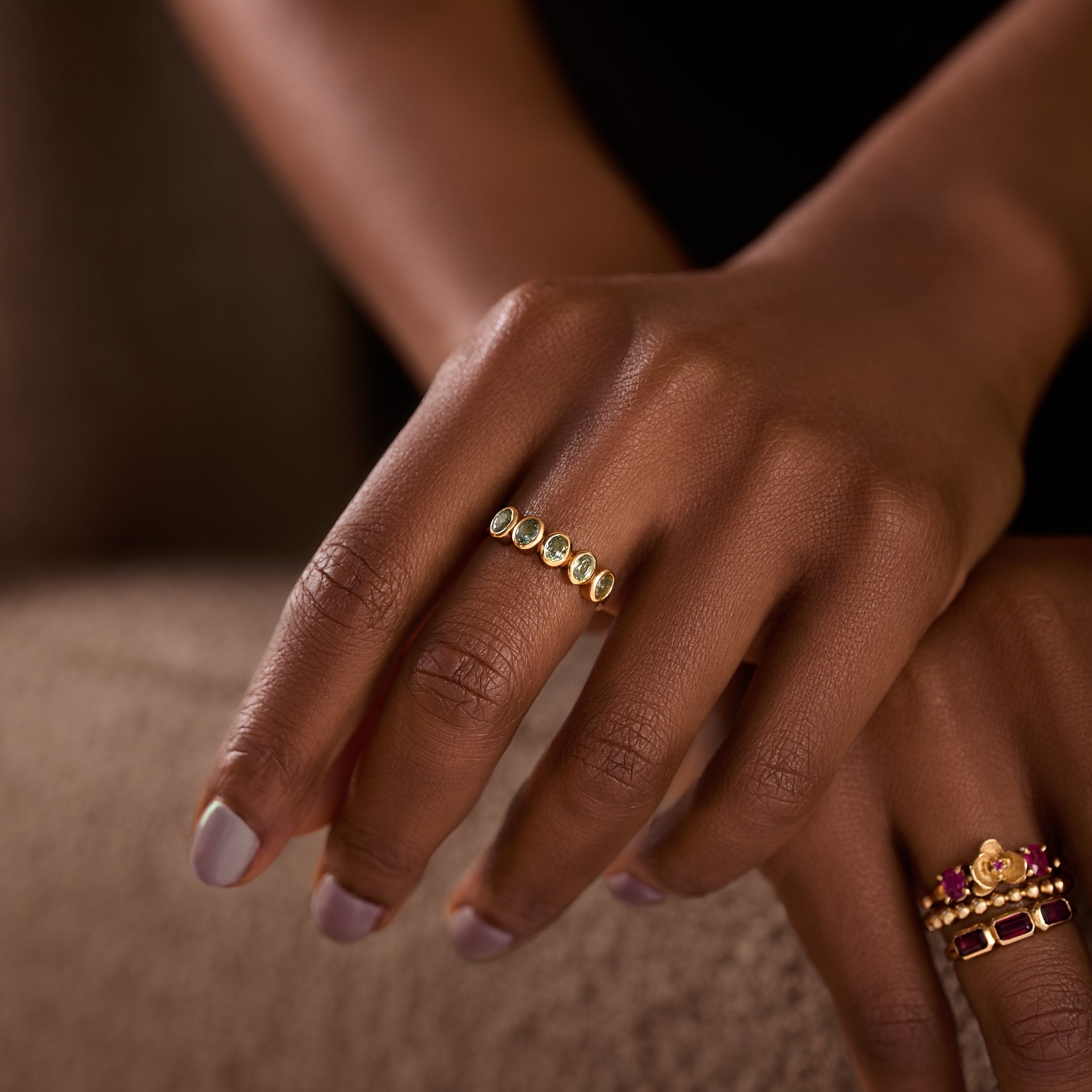 Close-up of a hand wearing a gold ring with green gemstones on a neutral background